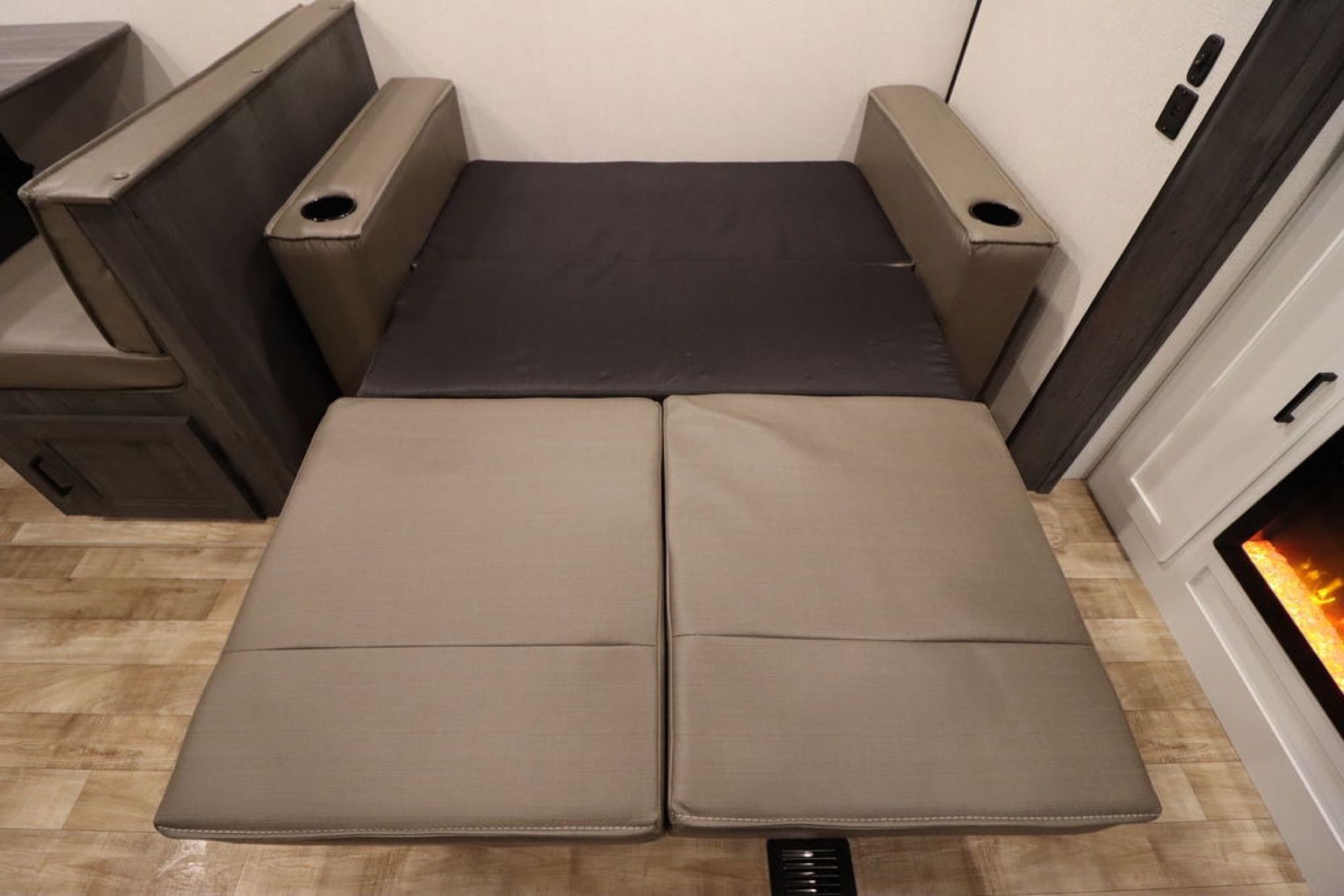 RV rental sofa bed extended into a sleeping area, featuring armrests with cupholders and dinette seating.. Keystone RV Hideout 2023