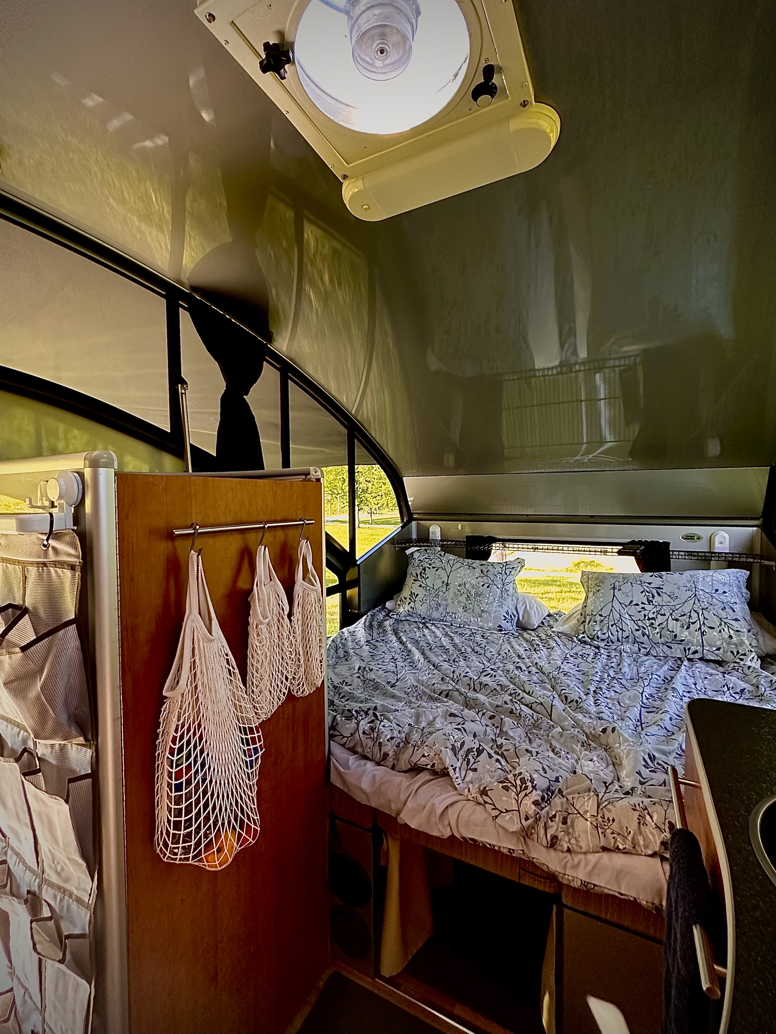 Inside a cozy rv rental: floral-patterned bed, overhead vent, practical hanging storage bags, and a glimpse of nature outside.. Safari Condo Alto R1713 2012