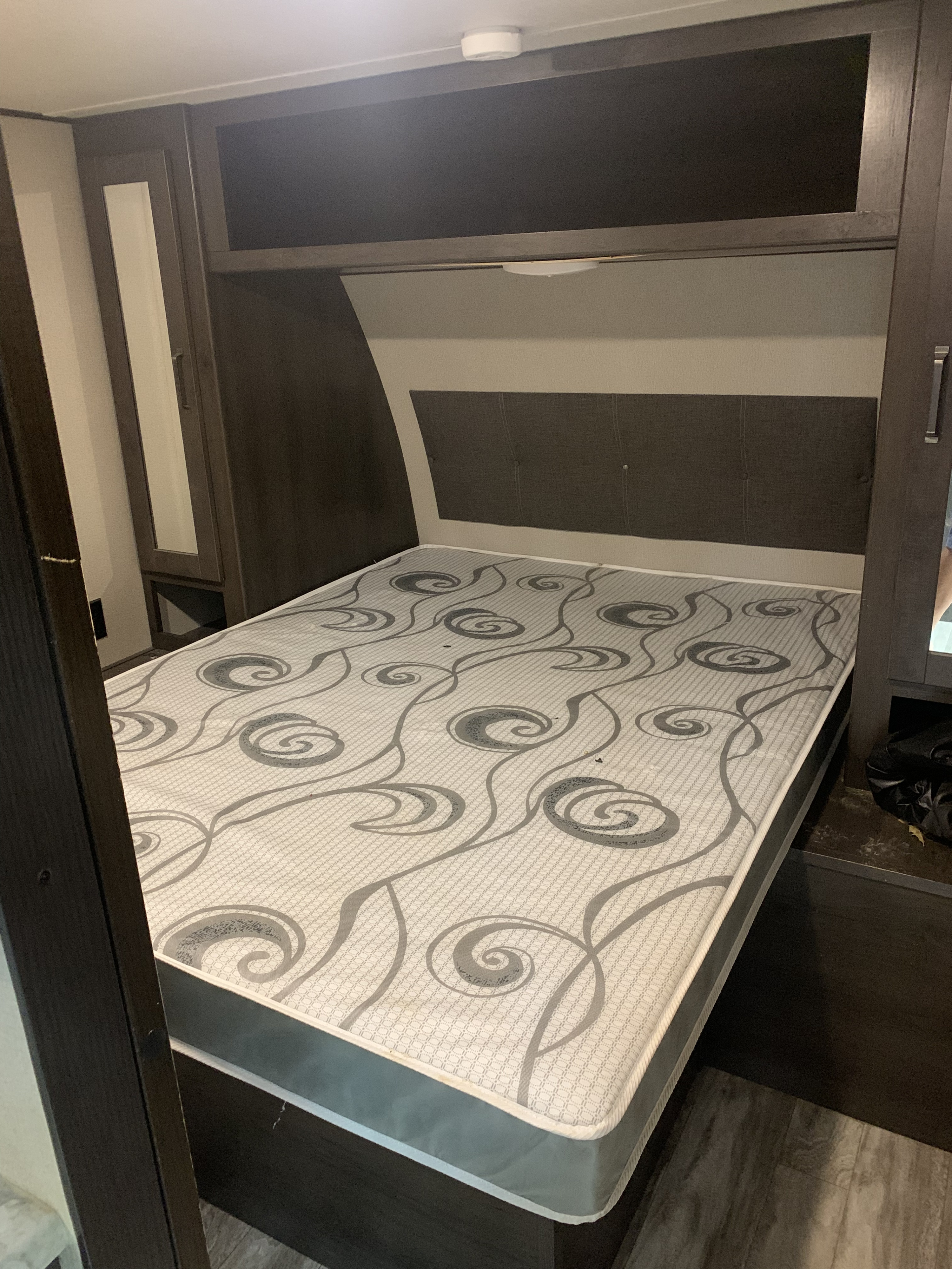 RV rental bedroom featuring a patterned mattress, built-in storage, and a padded headboard, ideal for travel.. Grand Design Transcend Xplor 2022