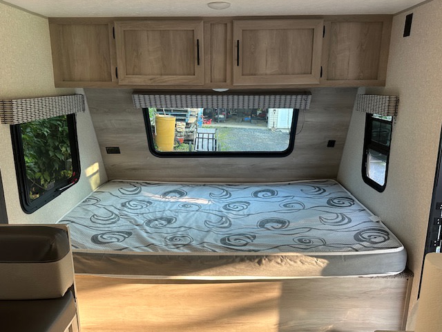 RV rental bedroom interior featuring a comfortable mattress, overhead cabinets, and bright windows.. KZ Classic 2022
