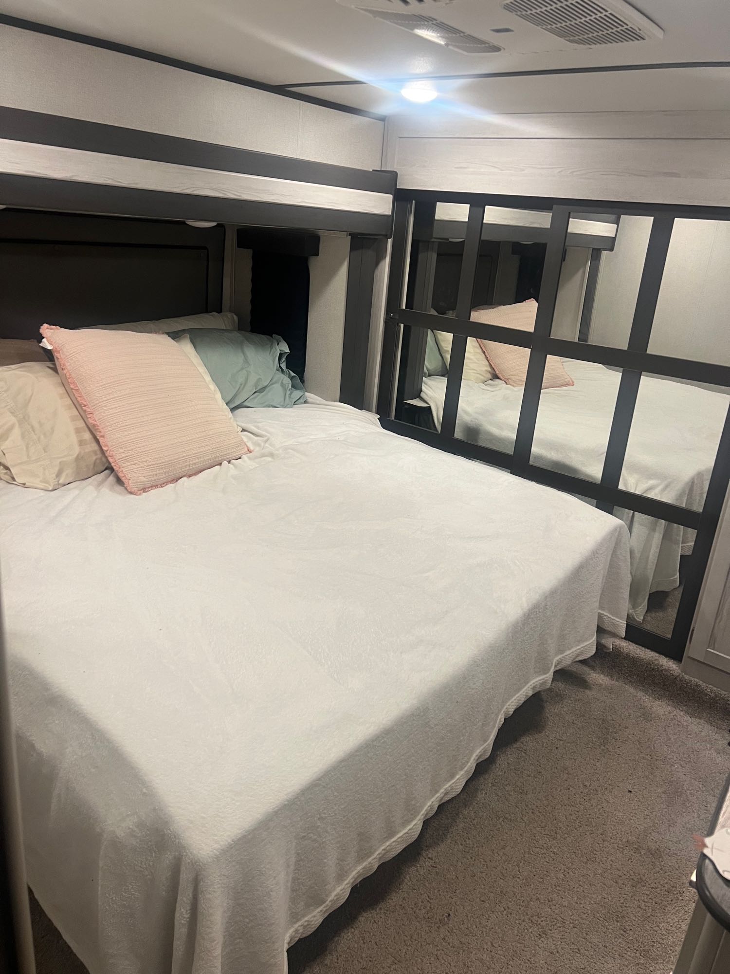 Inside an RV rental: a neat bedroom with a white bed, pillows, and an upper bunk, reflected in a mirrored wall.. Keystone RV Sprinter Limited 2022