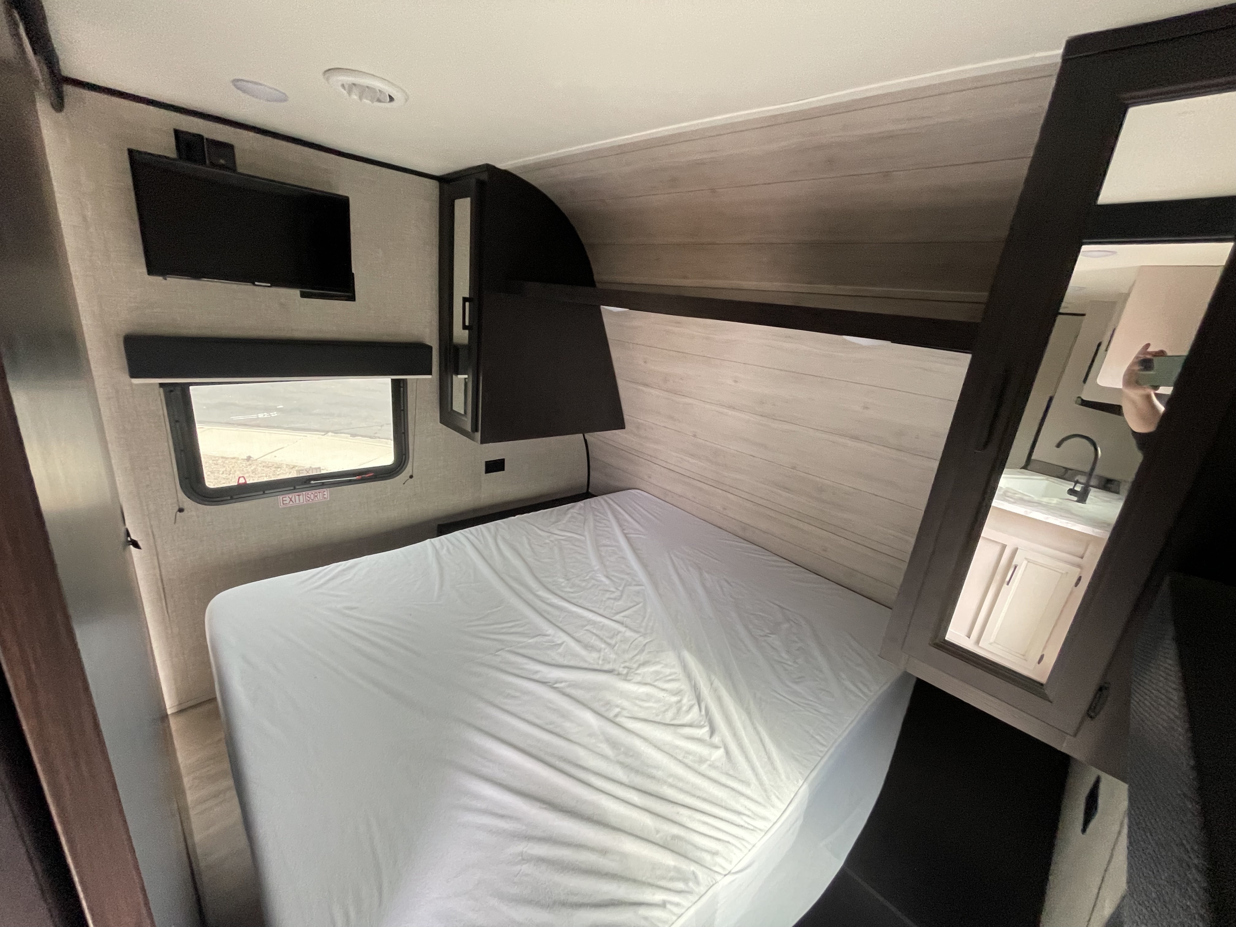 RV rental bedroom with a white bed, wall-mounted TV, and mirrored storage reflecting a sink and vanity.. Jayco Jay Flight SLX 2022