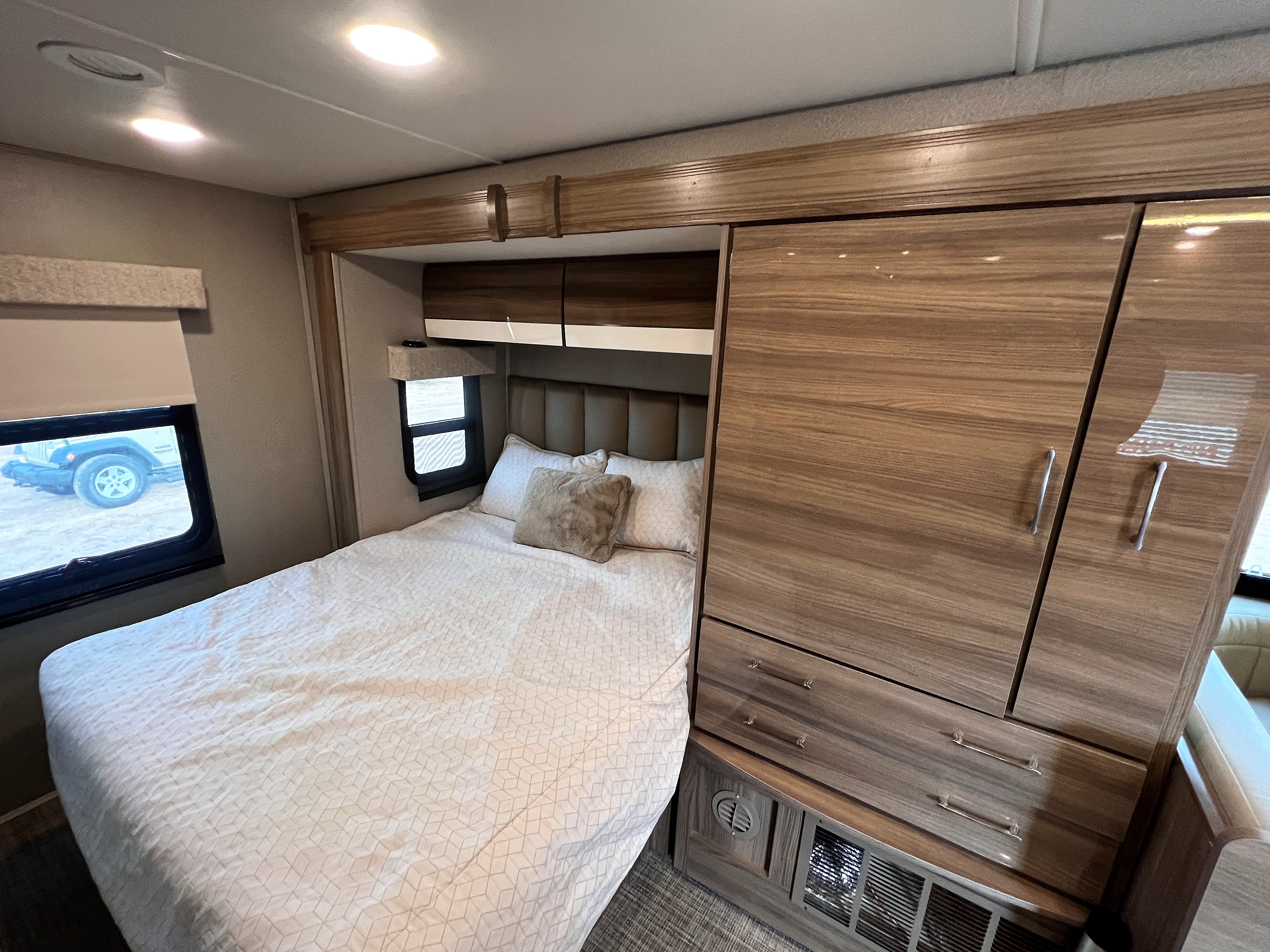 RV rental bedroom with a comfortable bed, window, overhead cabinets, and large wood storage unit.. Entegra Coach Qwest 2019