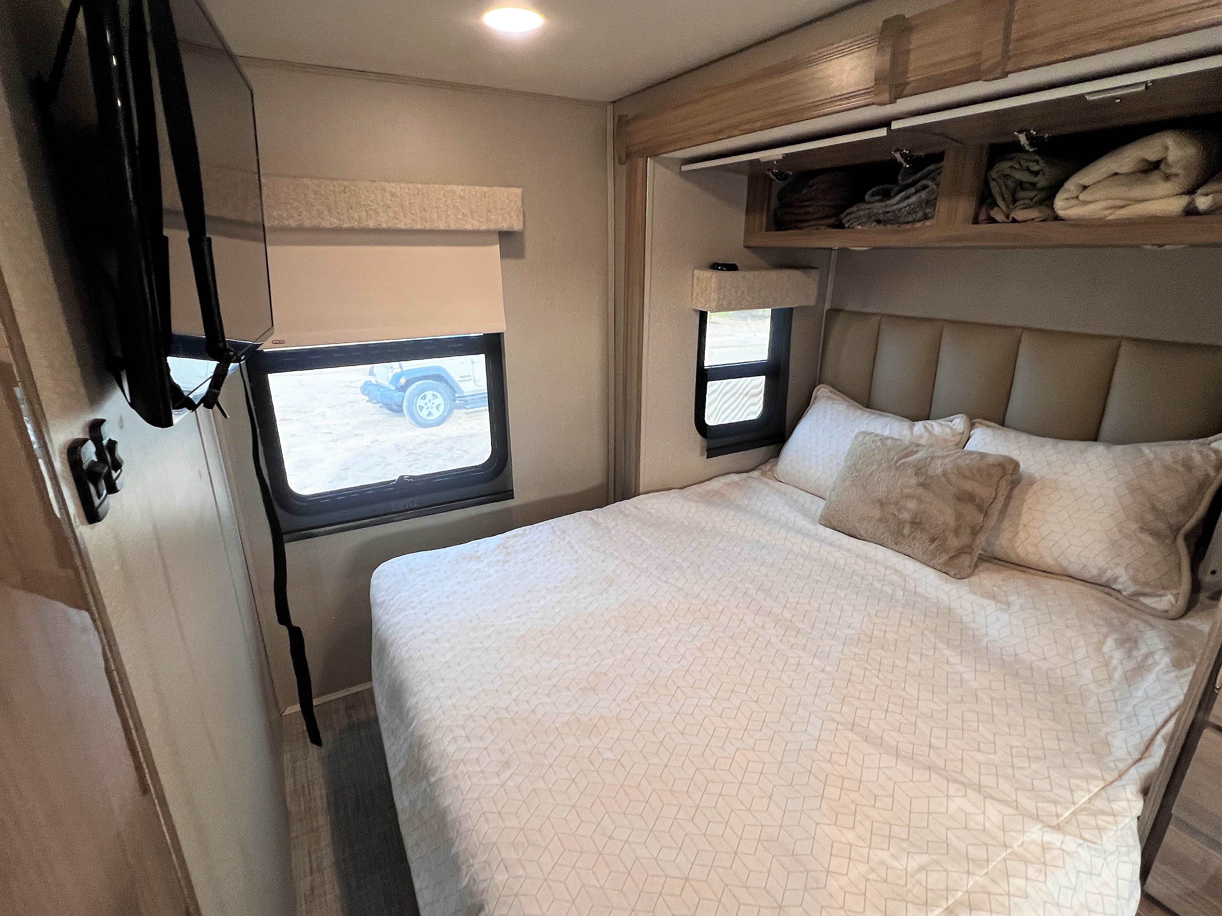 Experience comfort in this RV rental bedroom featuring a bed, TV, overhead storage, and windows.. Entegra Coach Qwest 2019