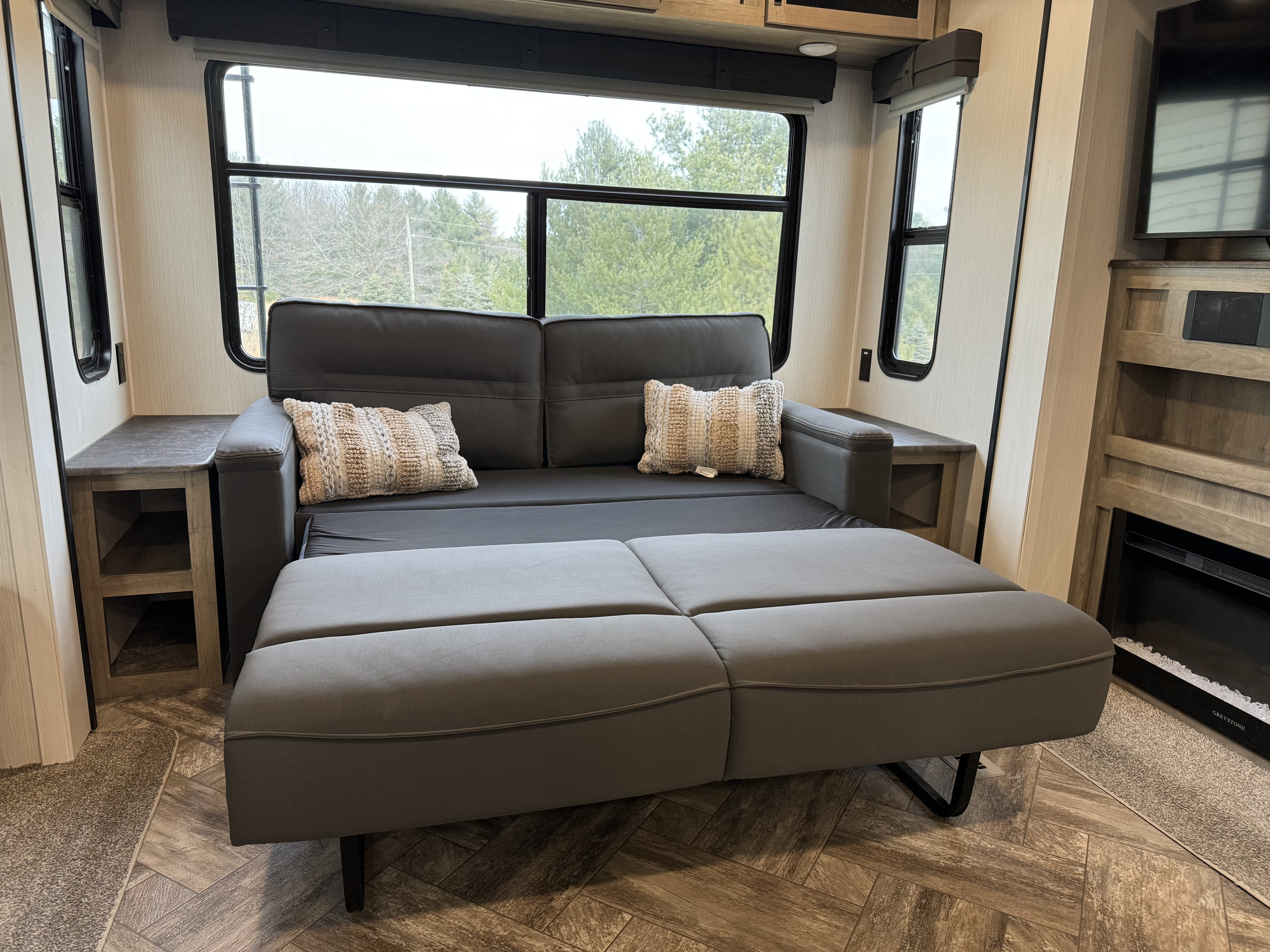 Spacious RV rental interior: gray convertible sofa/bed, side tables, large windows with nature view, and fireplace.. Palomino Puma 2023