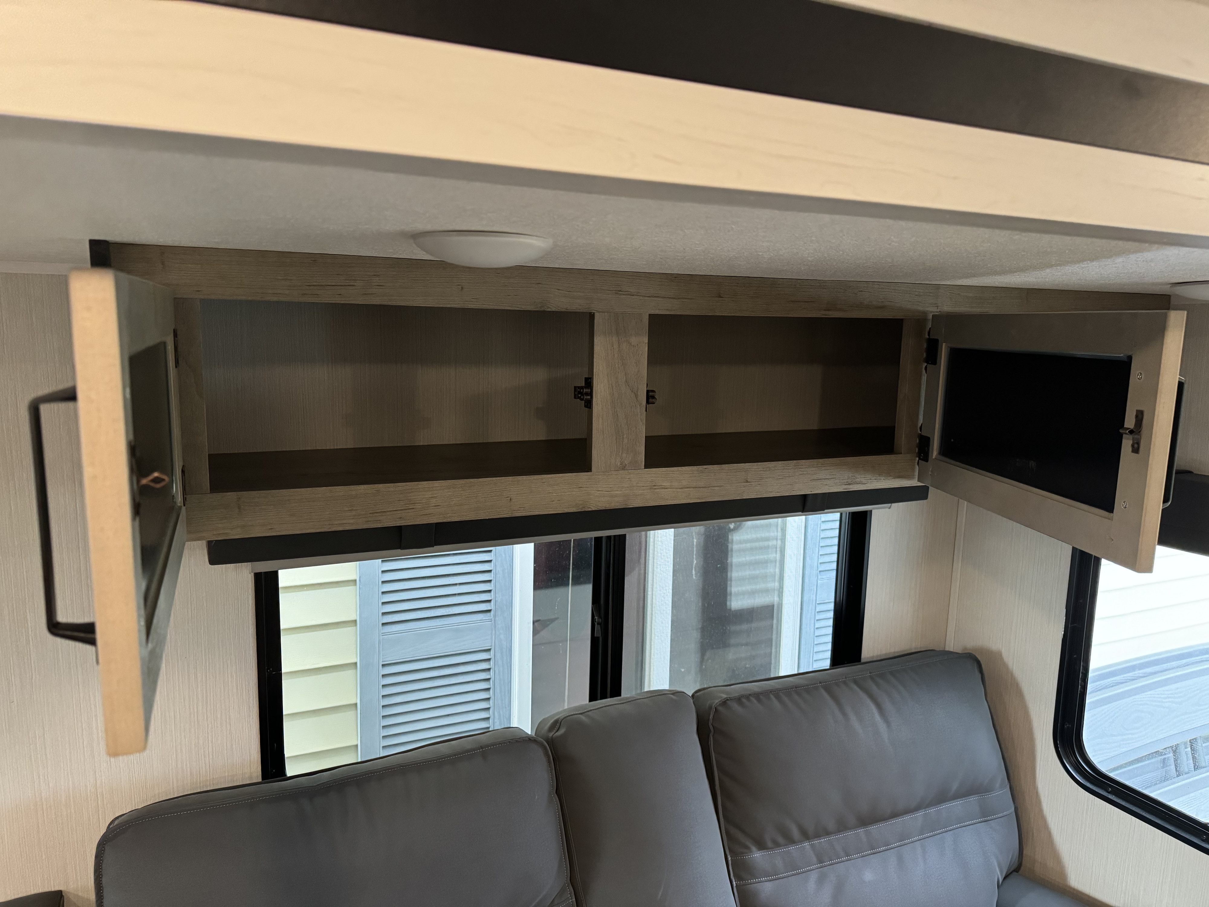 Inside an RV rental: open overhead storage cabinets, a window, and gray sofa seating.. Palomino Puma 2023