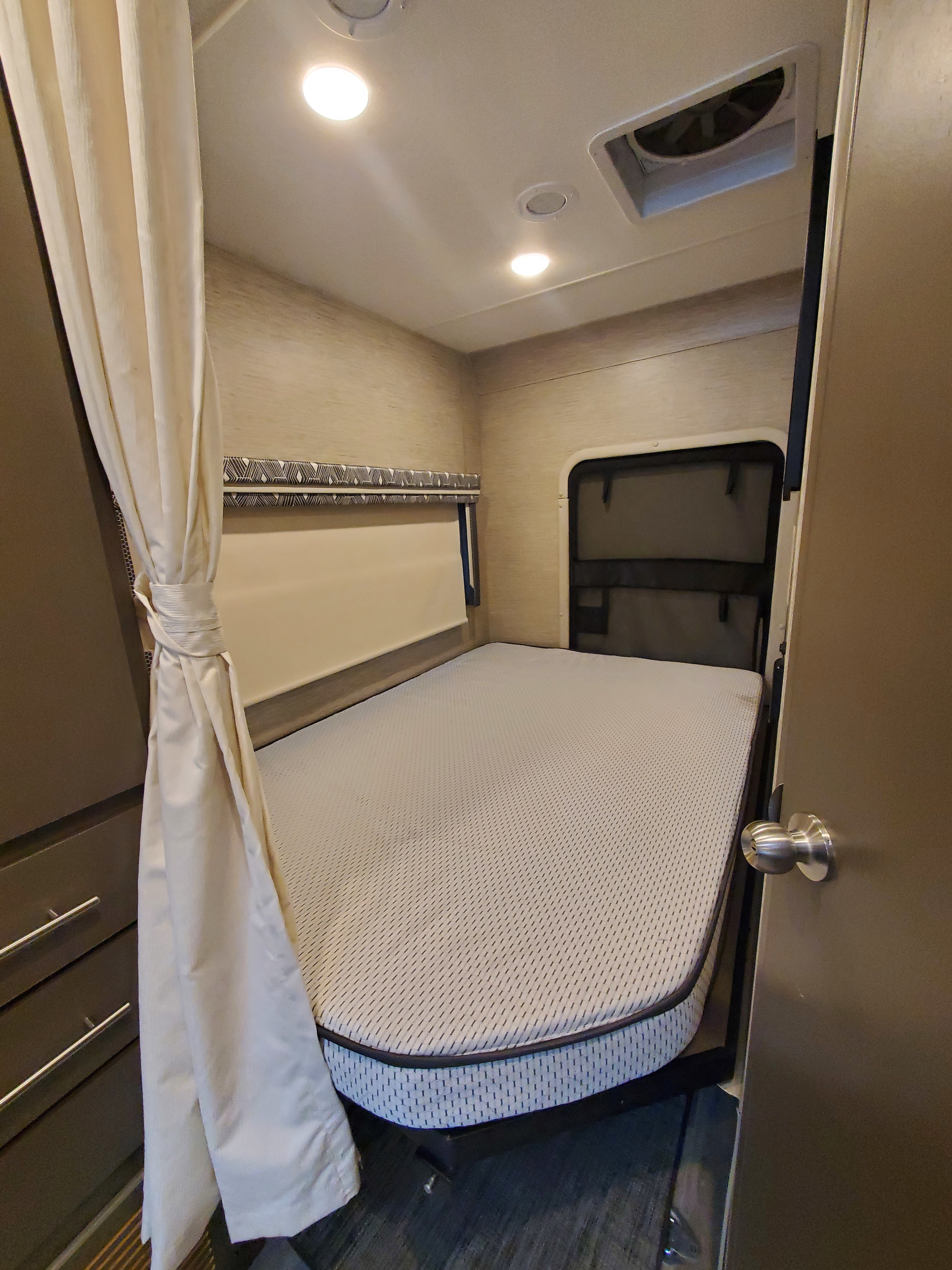 This RV rental's bedroom offers a comfortable bed, tied-back curtains, ceiling lights, and a vent for a pleasant stay.. Thor Motor Coach Axis 2023