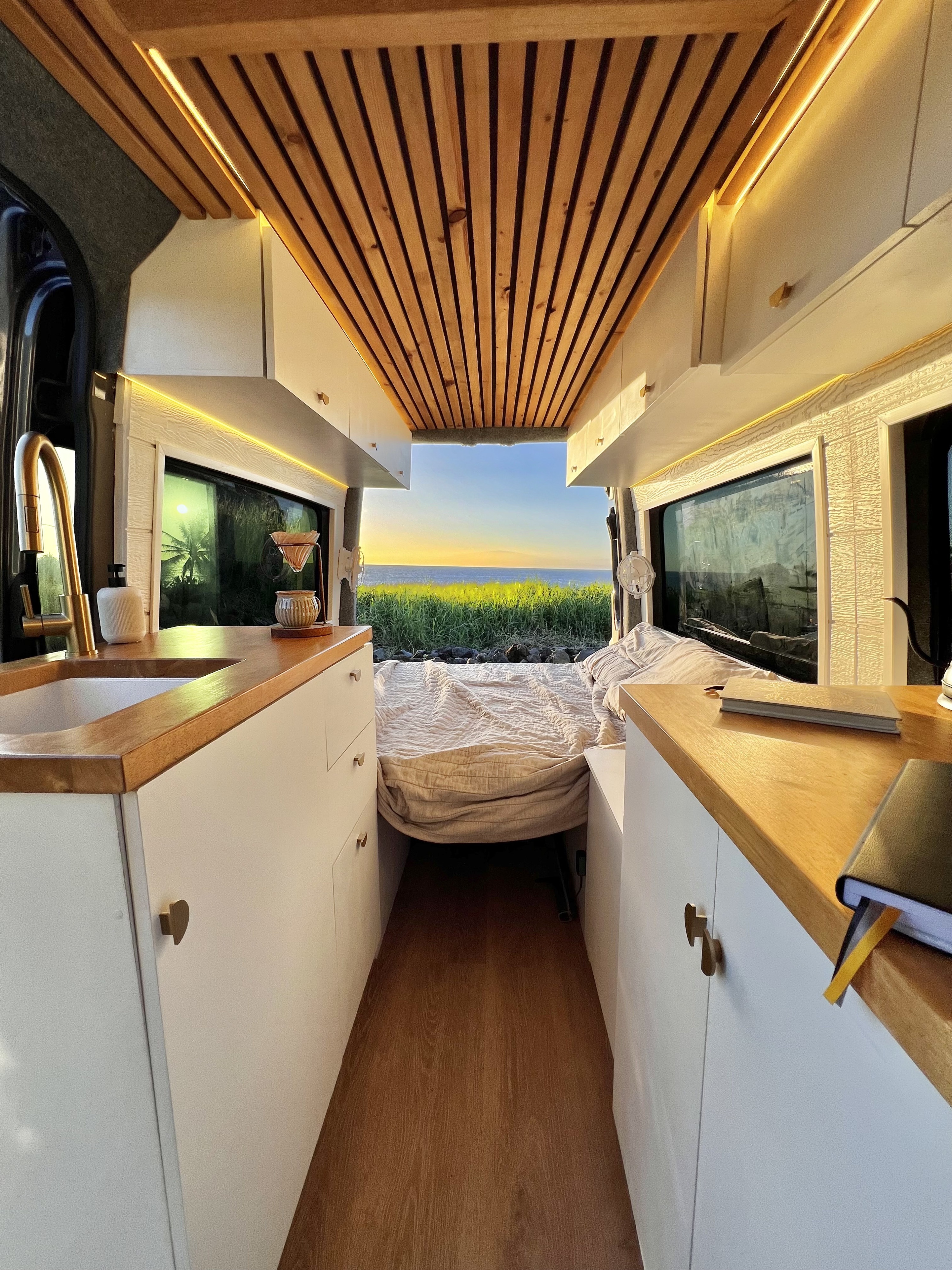 Cozy RV rental interior with wooden ceiling, functional kitchen & stunning ocean sunset view from the back. Perfect for van life adventures!. Mercedes-Benz Sprinter 2015