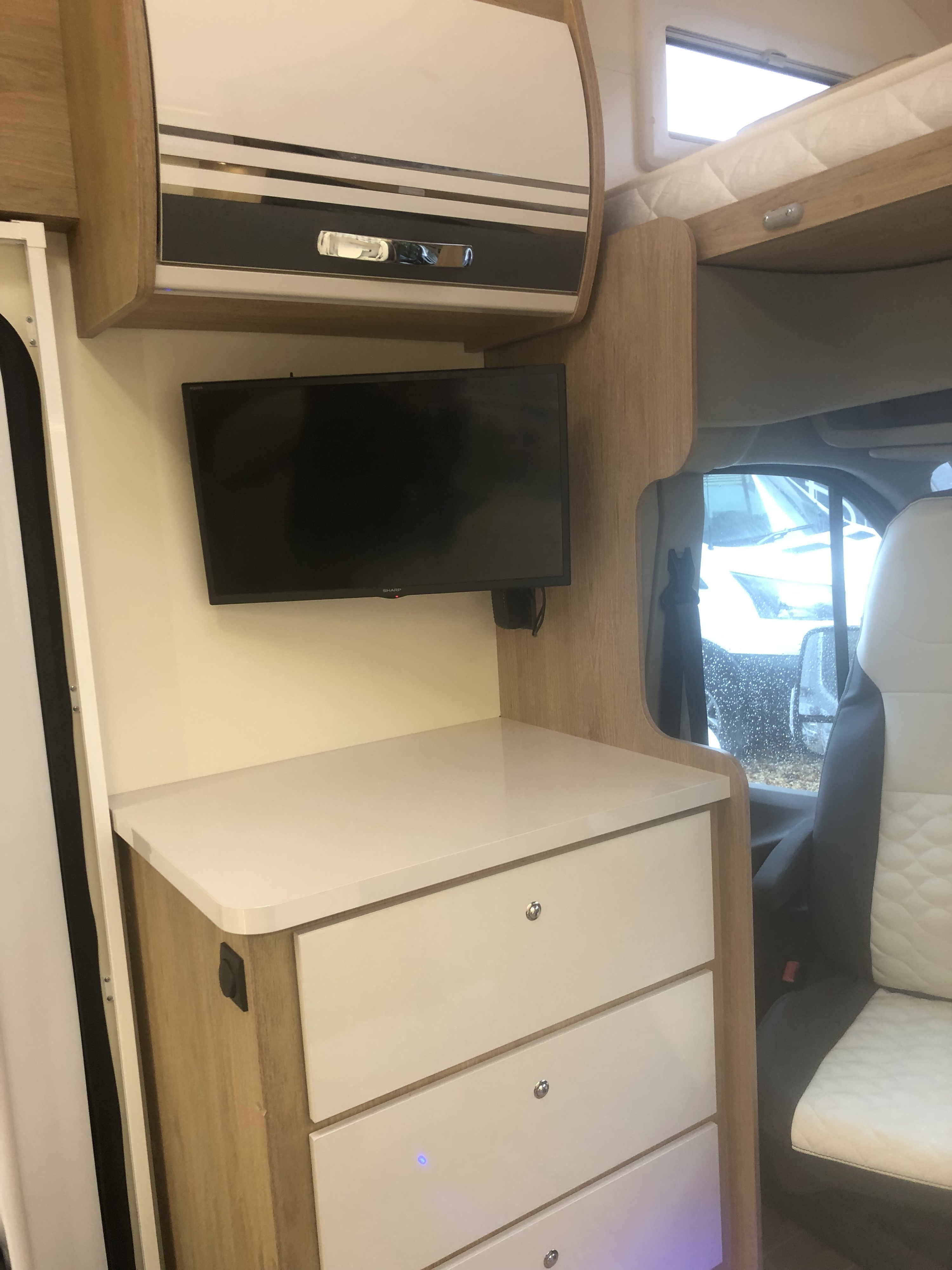 RV rental interior: A modern campervan cabin with a wall-mounted TV, white storage drawers, and an overhead bed.. Roller Team Auto Roller 746 2023