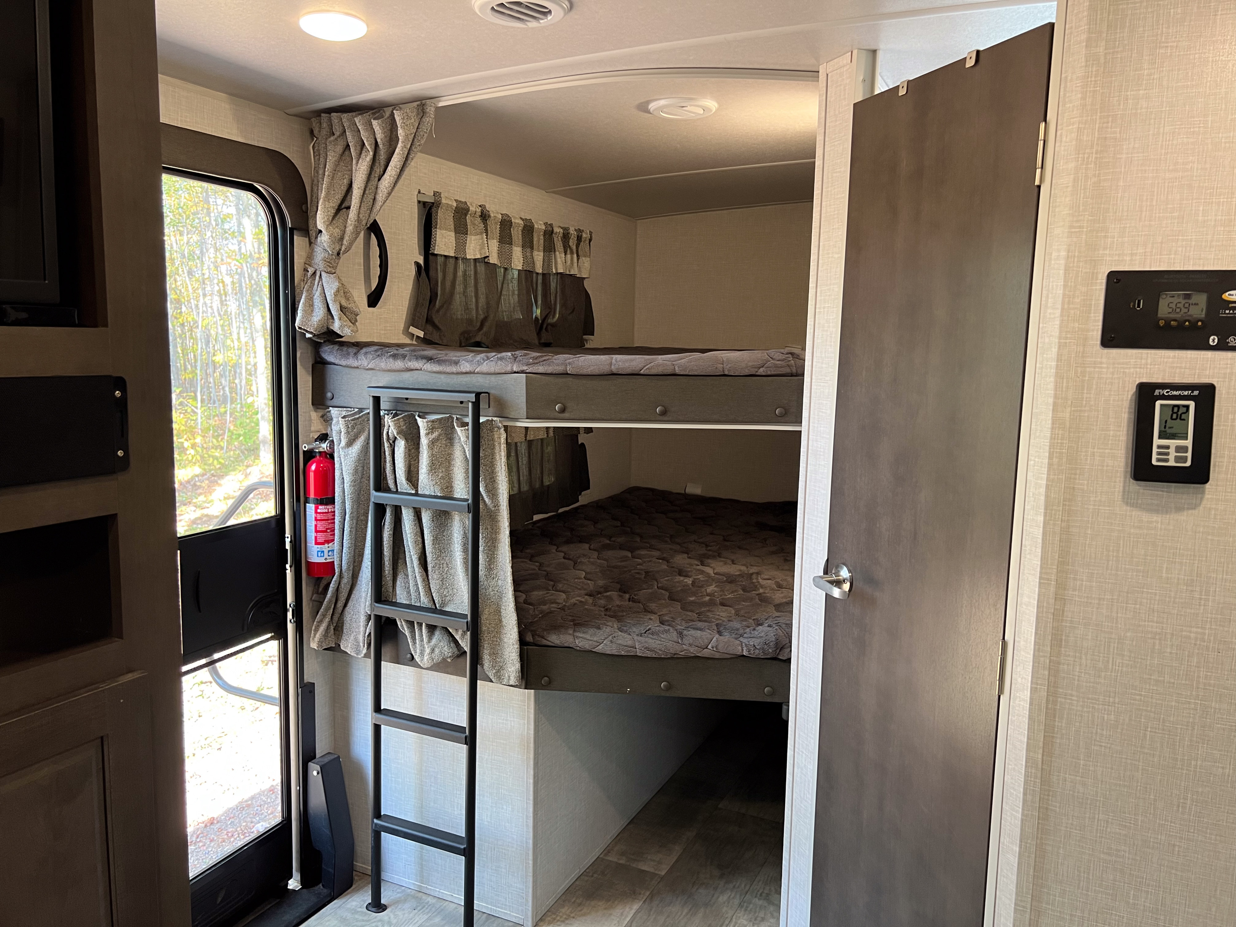 RV rental's functional interior: bunk beds with ladder, privacy curtains, and a fire extinguisher mounted by the door.. Forest River Flagstaff Super Lite 2021