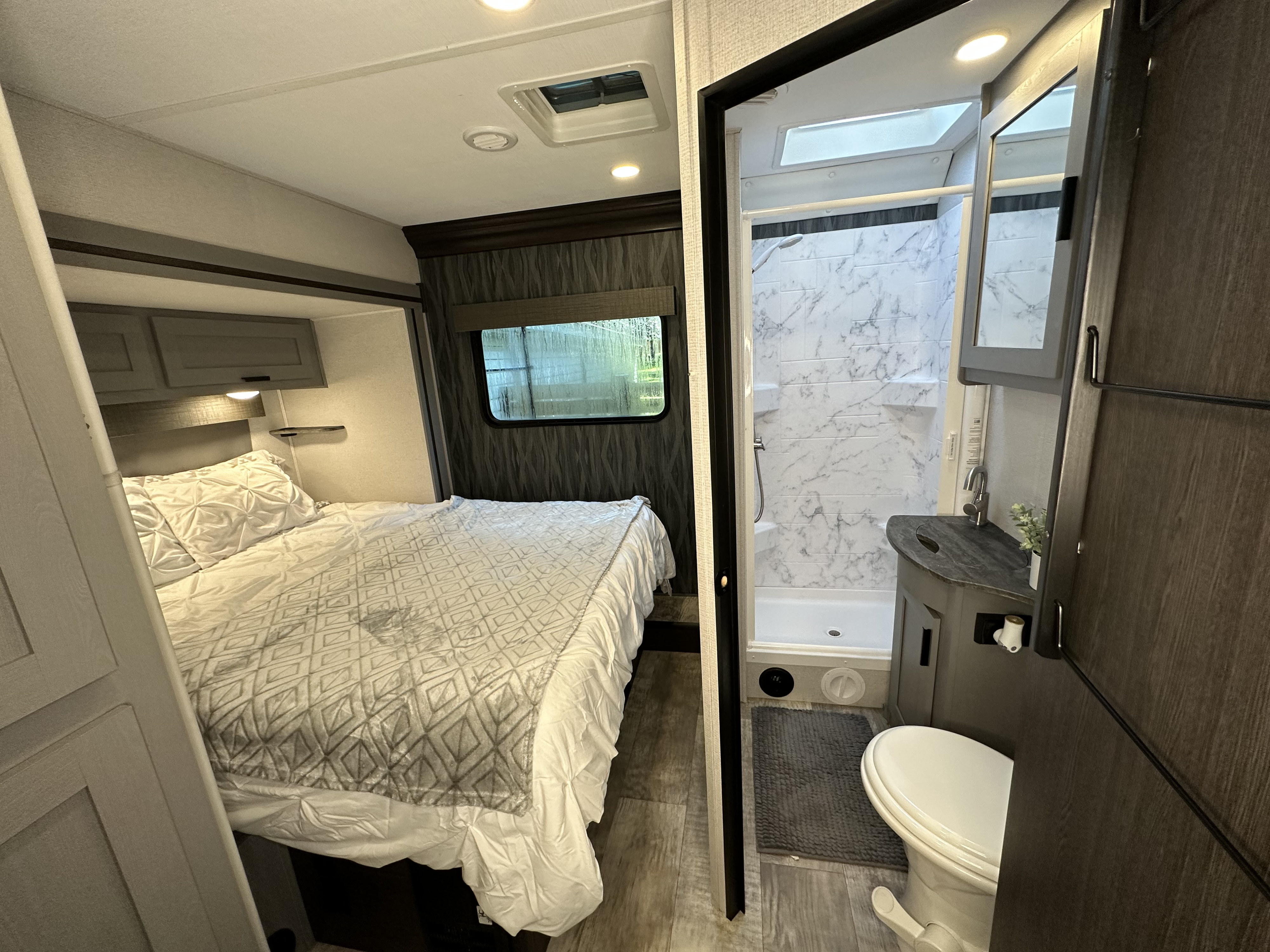 RV rental interior: cozy bedroom with bed & window, beside a full bathroom with shower, sink & toilet. Perfect for travel.. Forest River Solera 2021