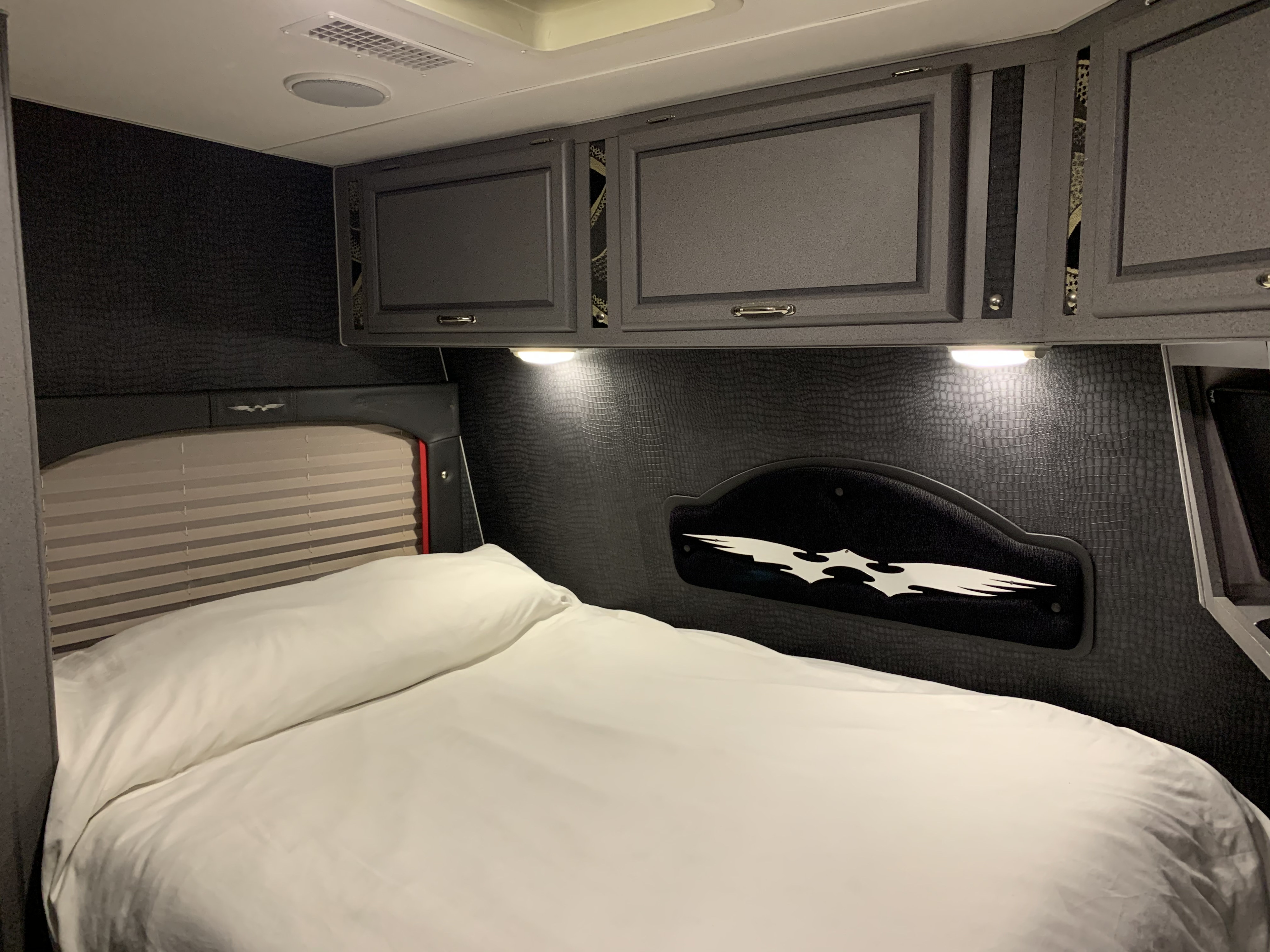 Inside a modern RV rental bedroom: dark textured walls, white bedding on a large bed, and functional overhead storage cabinets.. Weekend Warrior Super Lite 2007