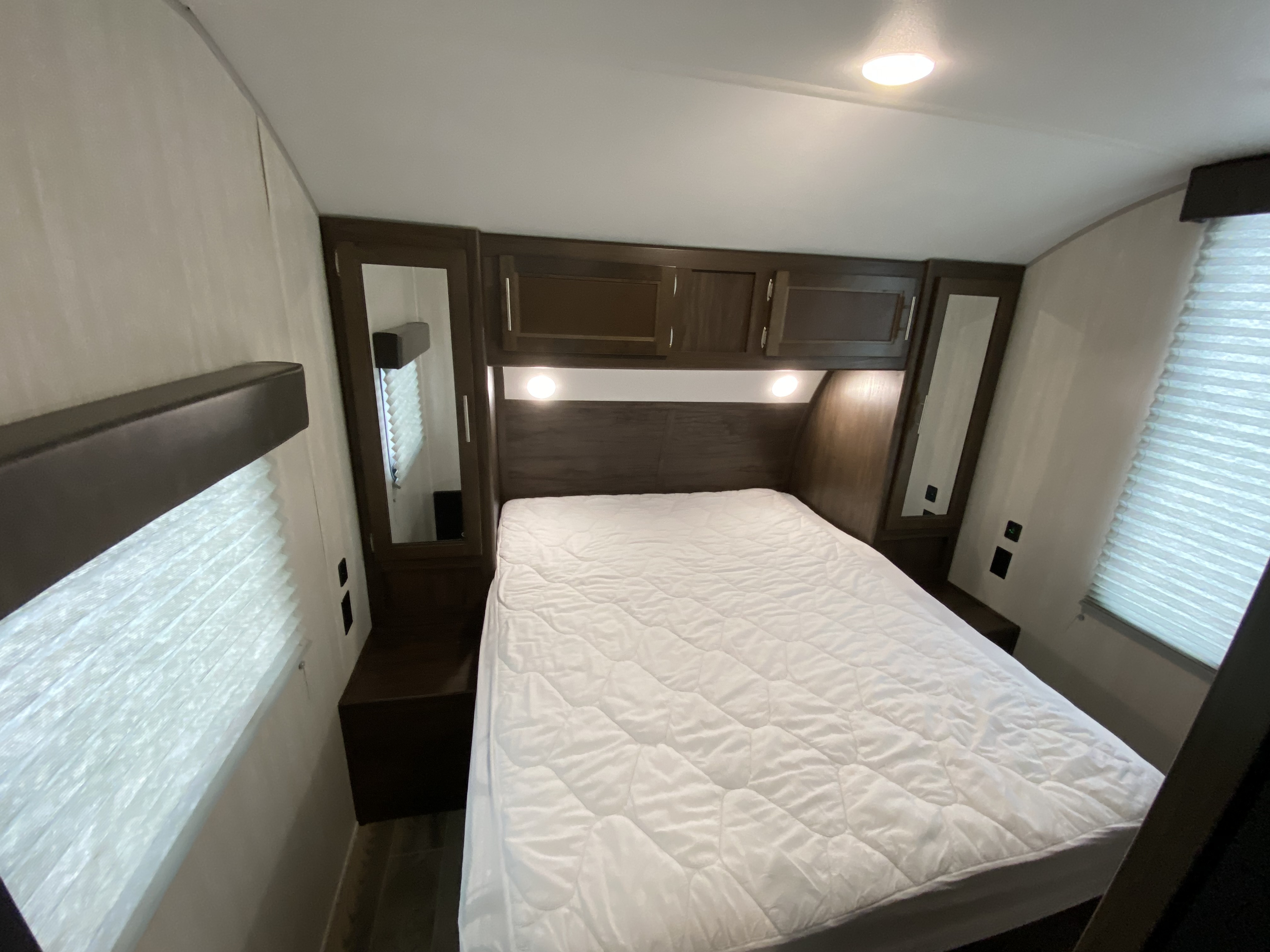 Step into a cozy RV rental bedroom featuring a comfortable bed, overhead cabinets, and soft lighting, ideal for travel.. Forest River Cherokee 2022