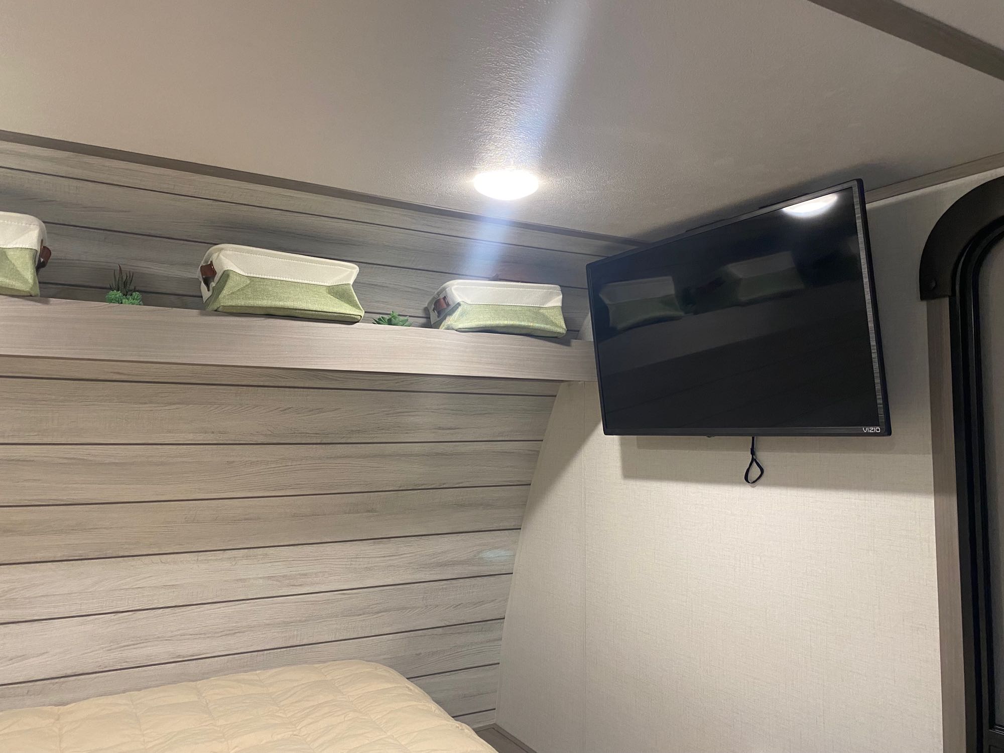 Cozy RV rental bedroom with modern wood paneling, overhead storage, and a wall-mounted TV. Perfect for your next adventure!. Dutchmen Coleman Lantern LT 2023
