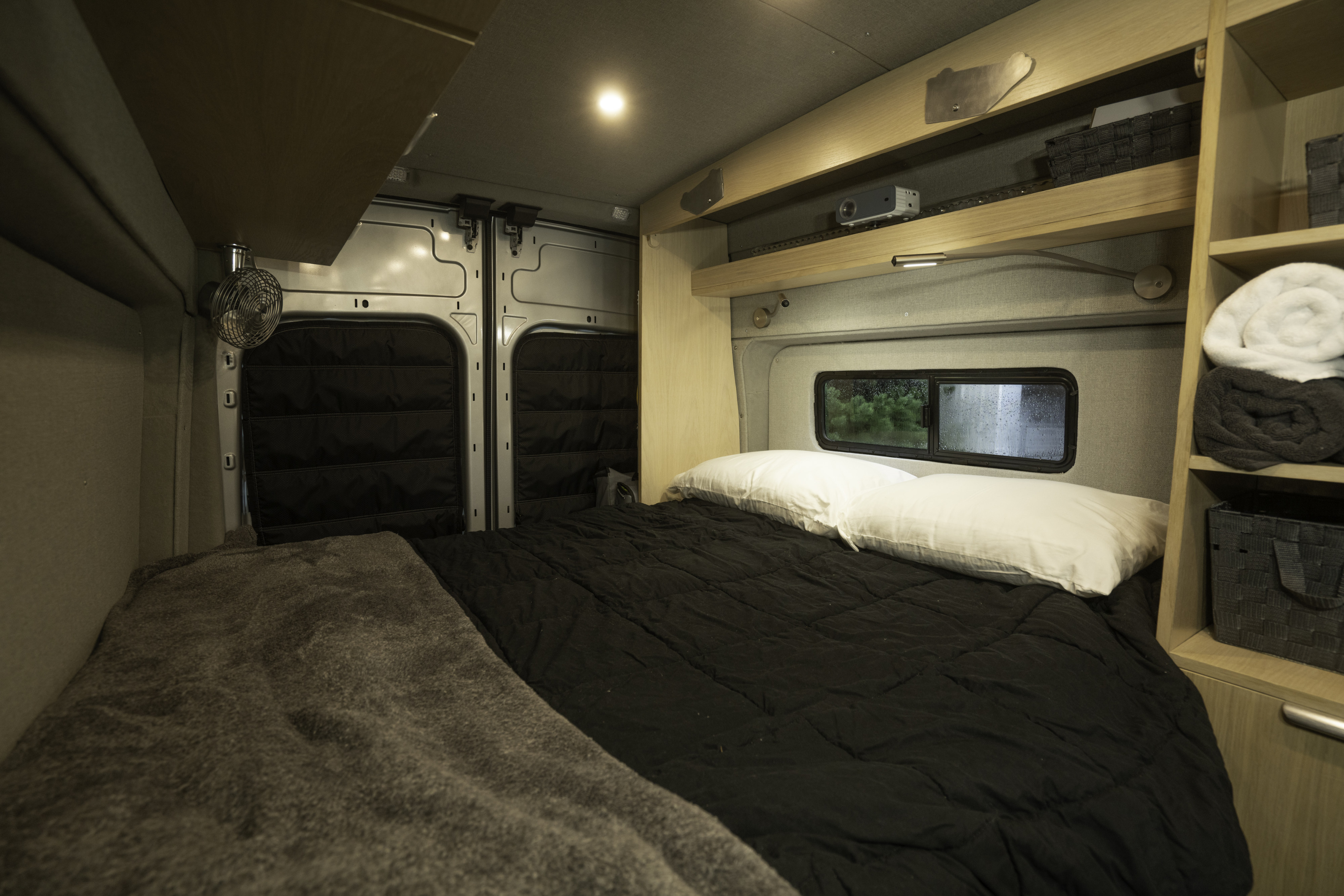 Cozy RV rental bedroom with black bedding, a fan, and smart storage shelves for comfortable travel.. Ford Custom Transit 2021