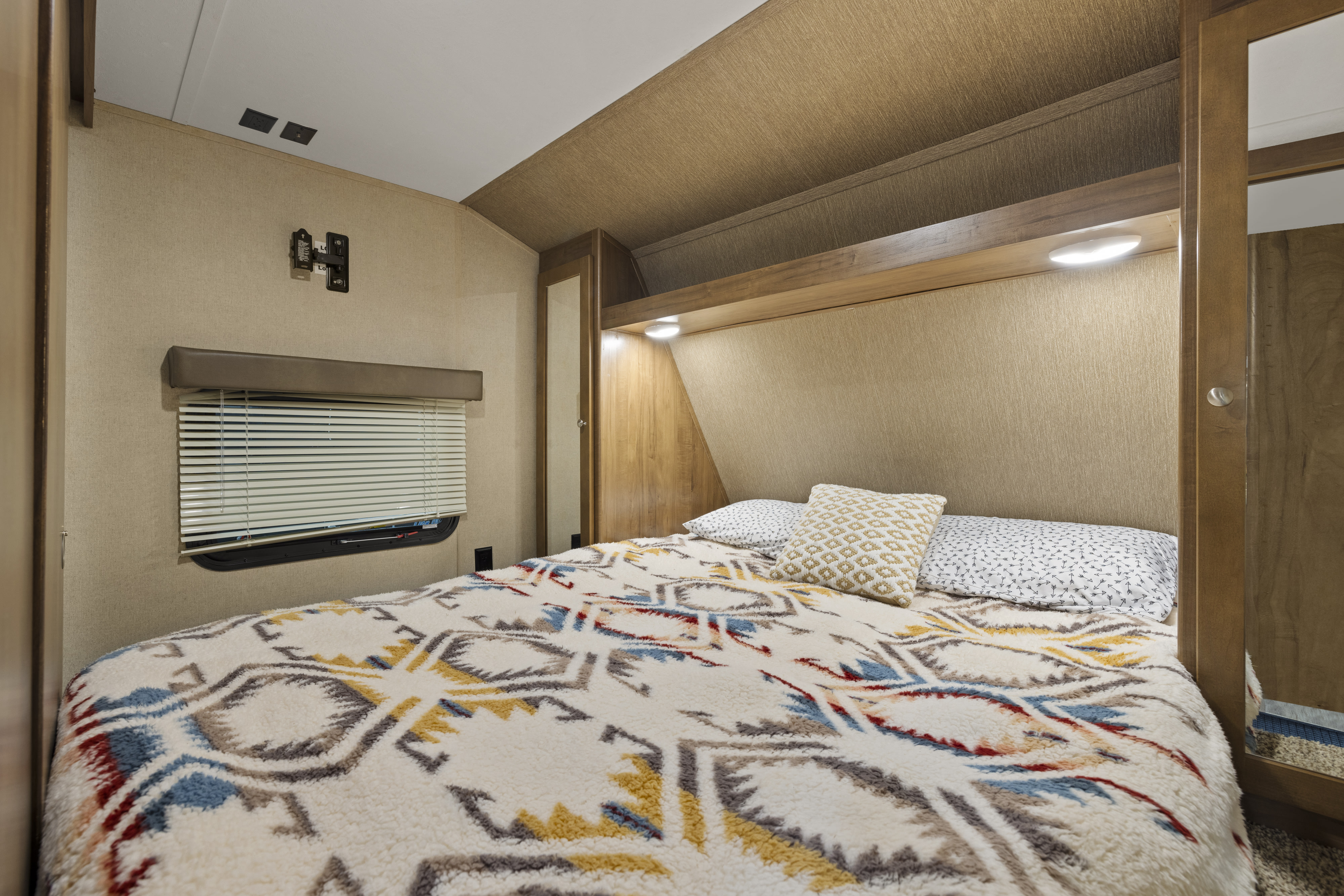 Cozy RV rental bedroom with patterned blanket, built-in lighting, and window. Perfect for travel.. Aspen Trail Dutchman 2017
