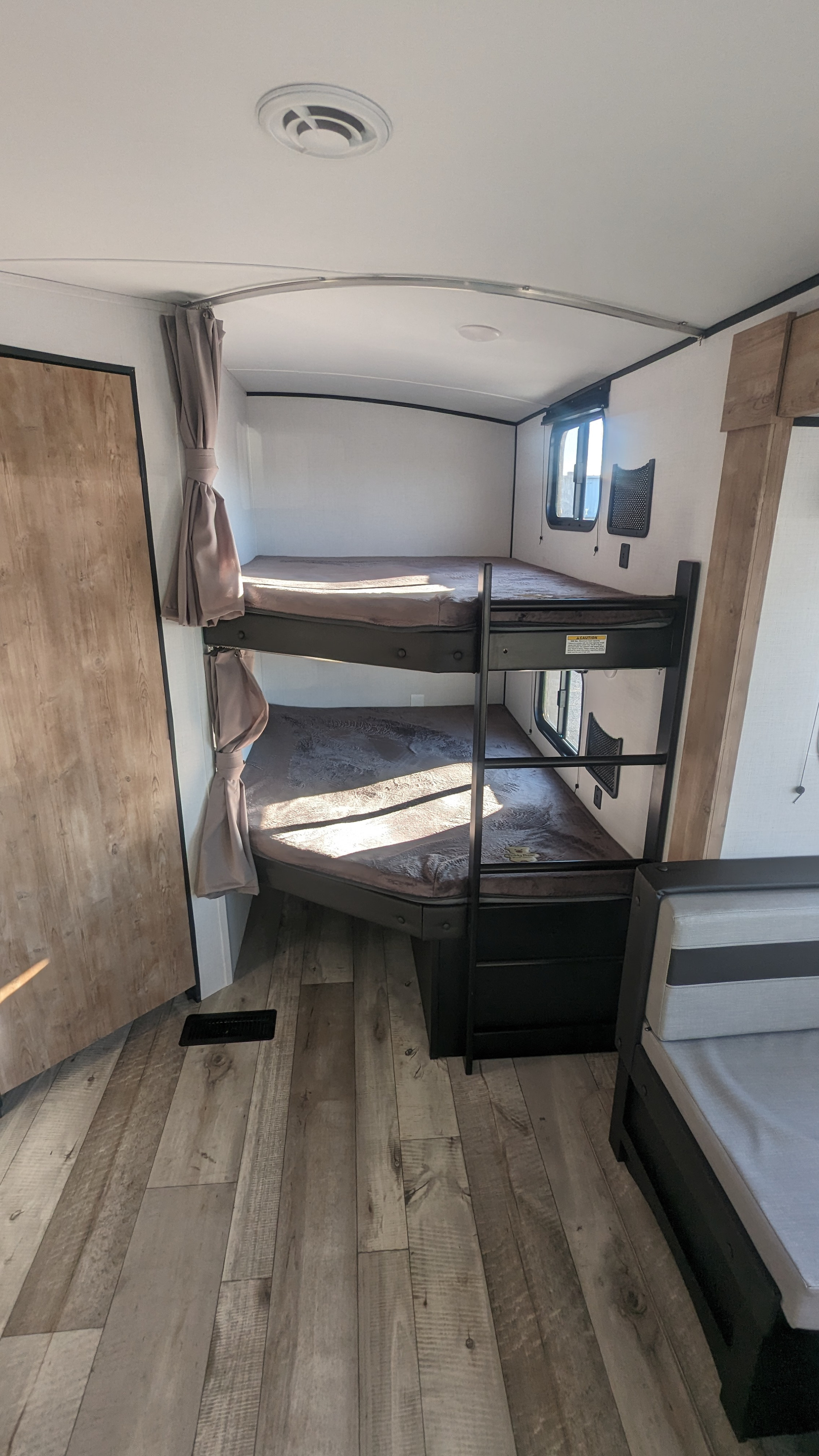 RV rental's cozy interior: Stacked bunk beds with privacy curtains, wood-look flooring, and a functional sleeping area.. Keystone RV Springdale 2023