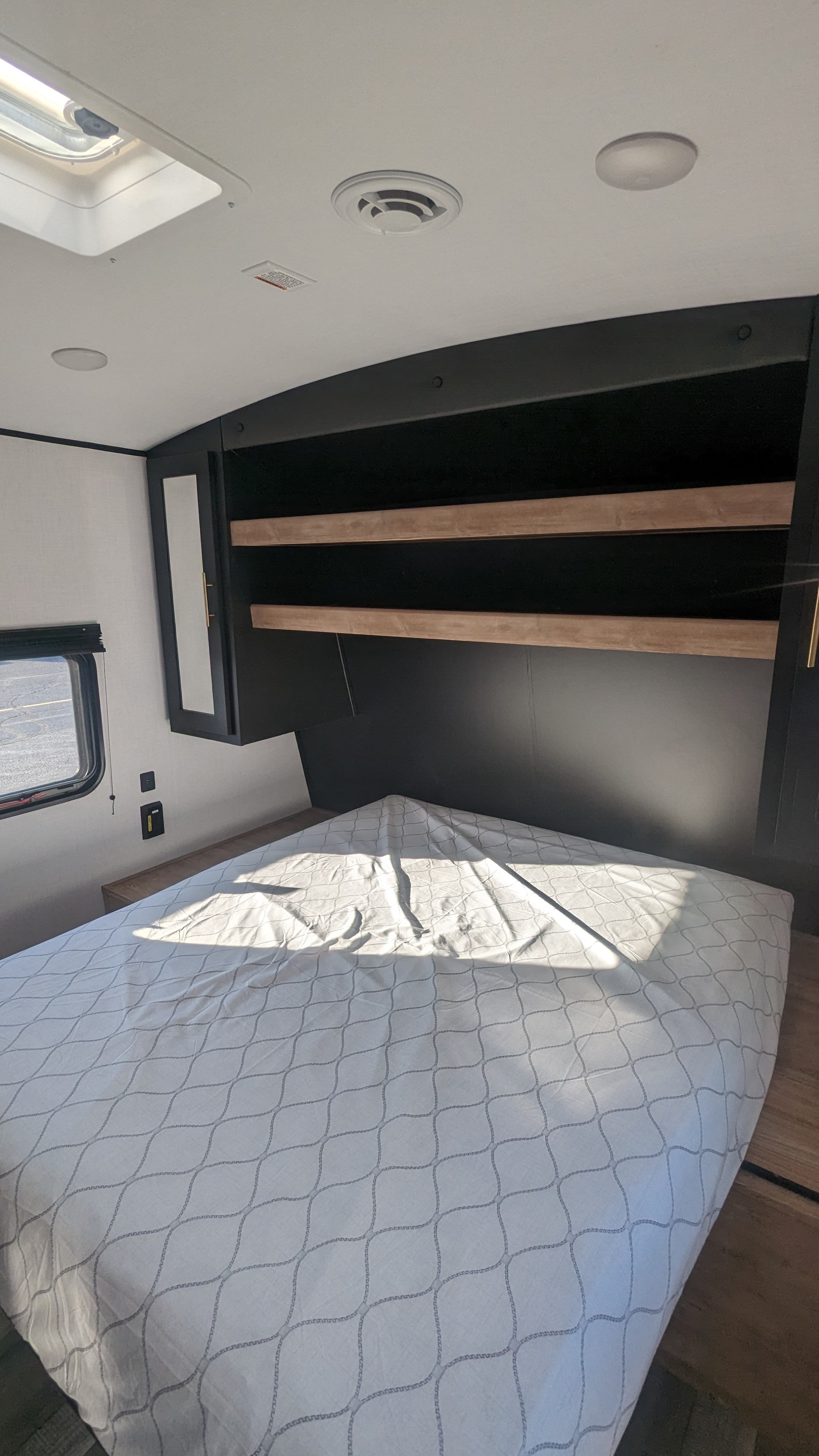 Spacious RV rental bedroom featuring a comfortable bed, overhead storage, and a sunlit interior with a skylight and window.. Keystone RV Springdale 2023