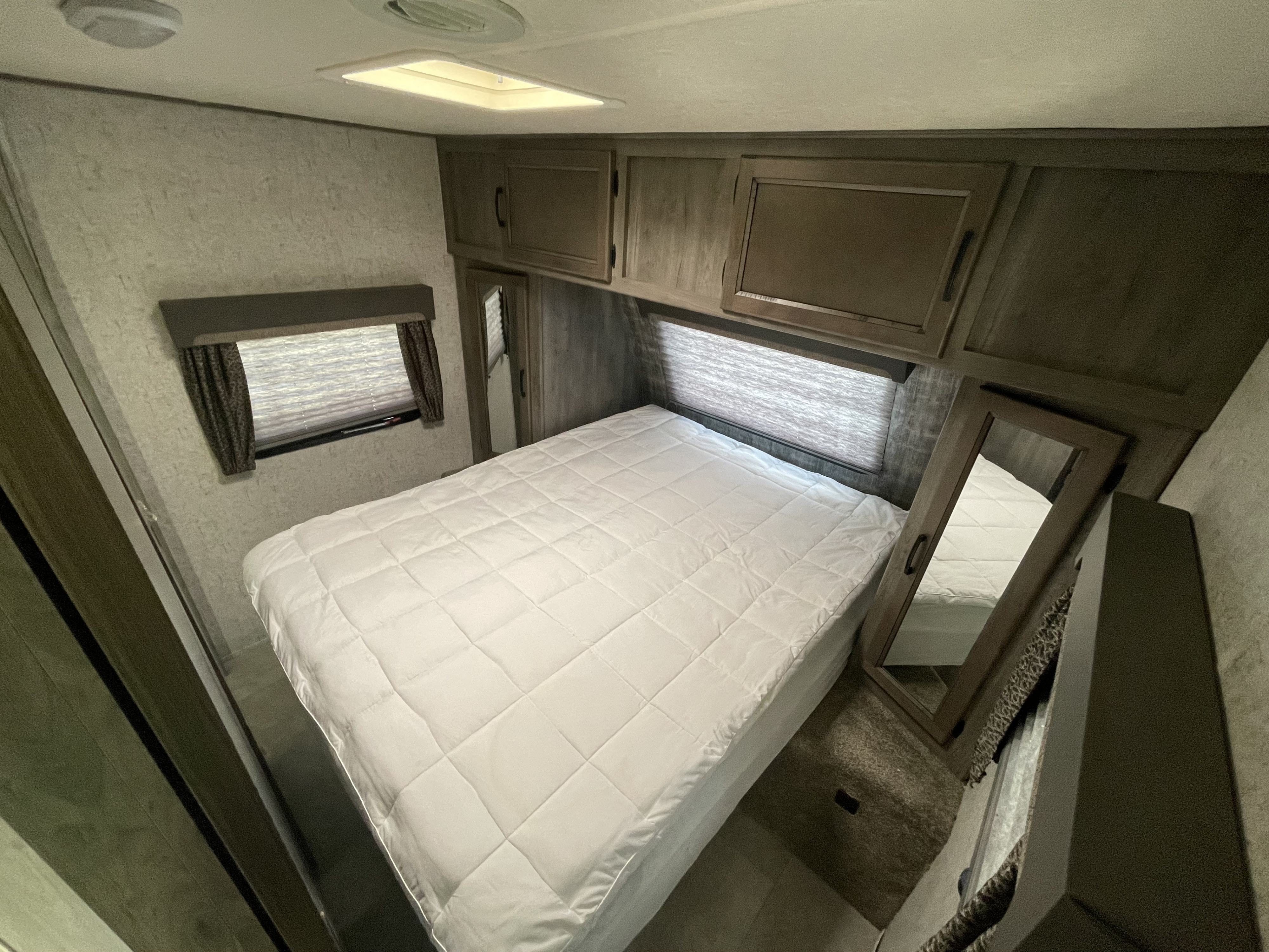 Cozy RV rental bedroom featuring a comfortable bed, overhead cabinets, and a window for natural light.. Coachmen Apex 2019