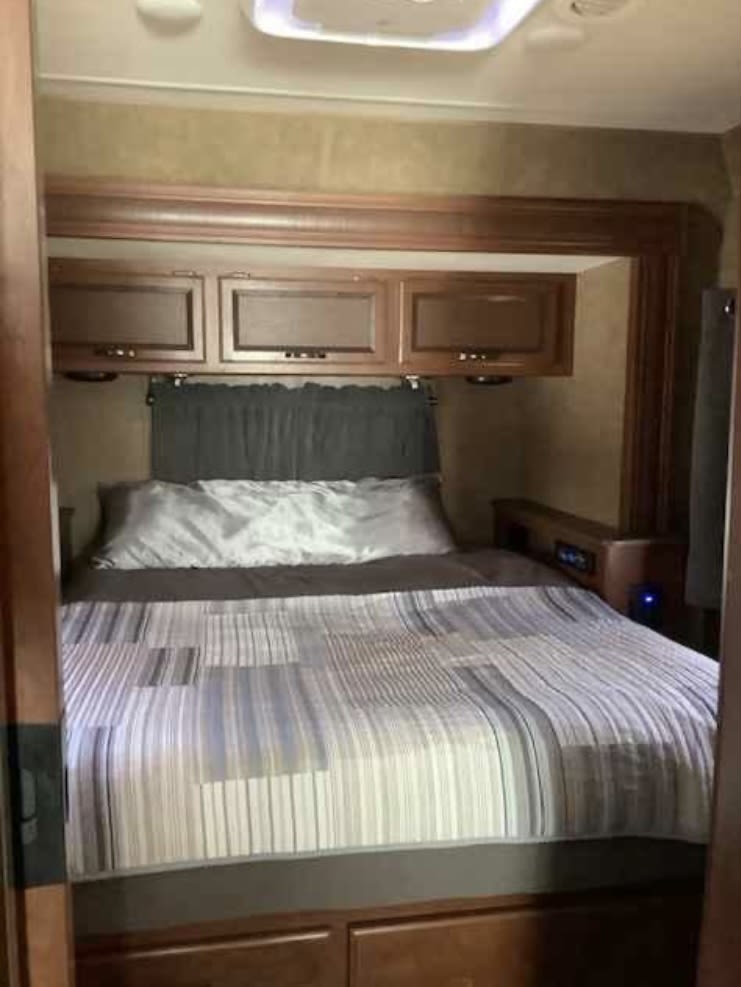 Inside an RV rental: a cozy bedroom featuring a bed with striped comforter and overhead wooden cabinets.. Thor Vegas 2016