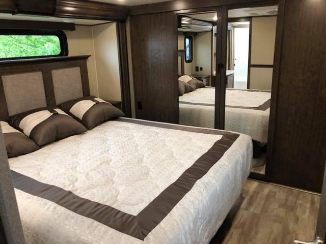 Cozy RV rental bedroom with a large bed, side window, and mirrored closet, offering comfortable mobile living.. Grand Design Solitude 2019