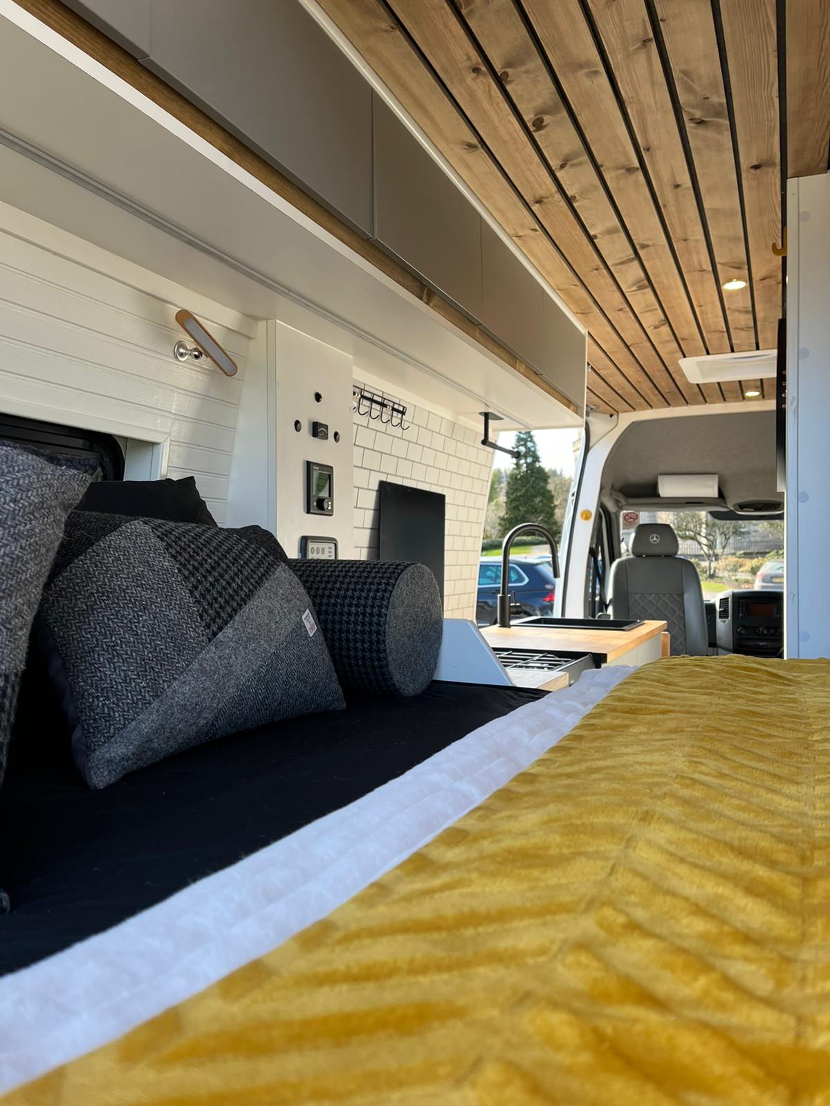 Inside a premium RV rental: comfortable bed, functional kitchen, and stylish wood ceiling in a modern campervan.. Mercedes-Benz Sprinter 2015