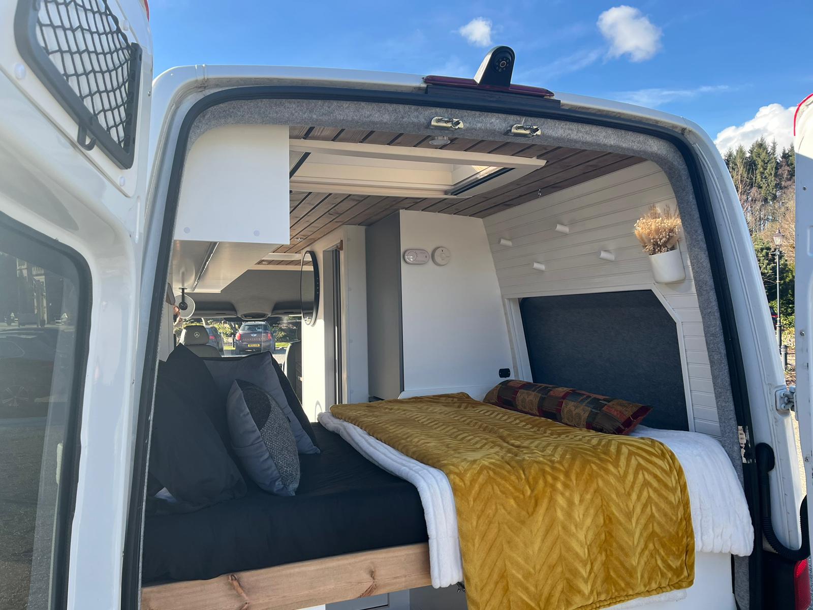 Cozy RV rental interior: A converted camper van with a comfortable bed, wood ceiling, skylight, and open rear doors.. Mercedes-Benz Sprinter 2015