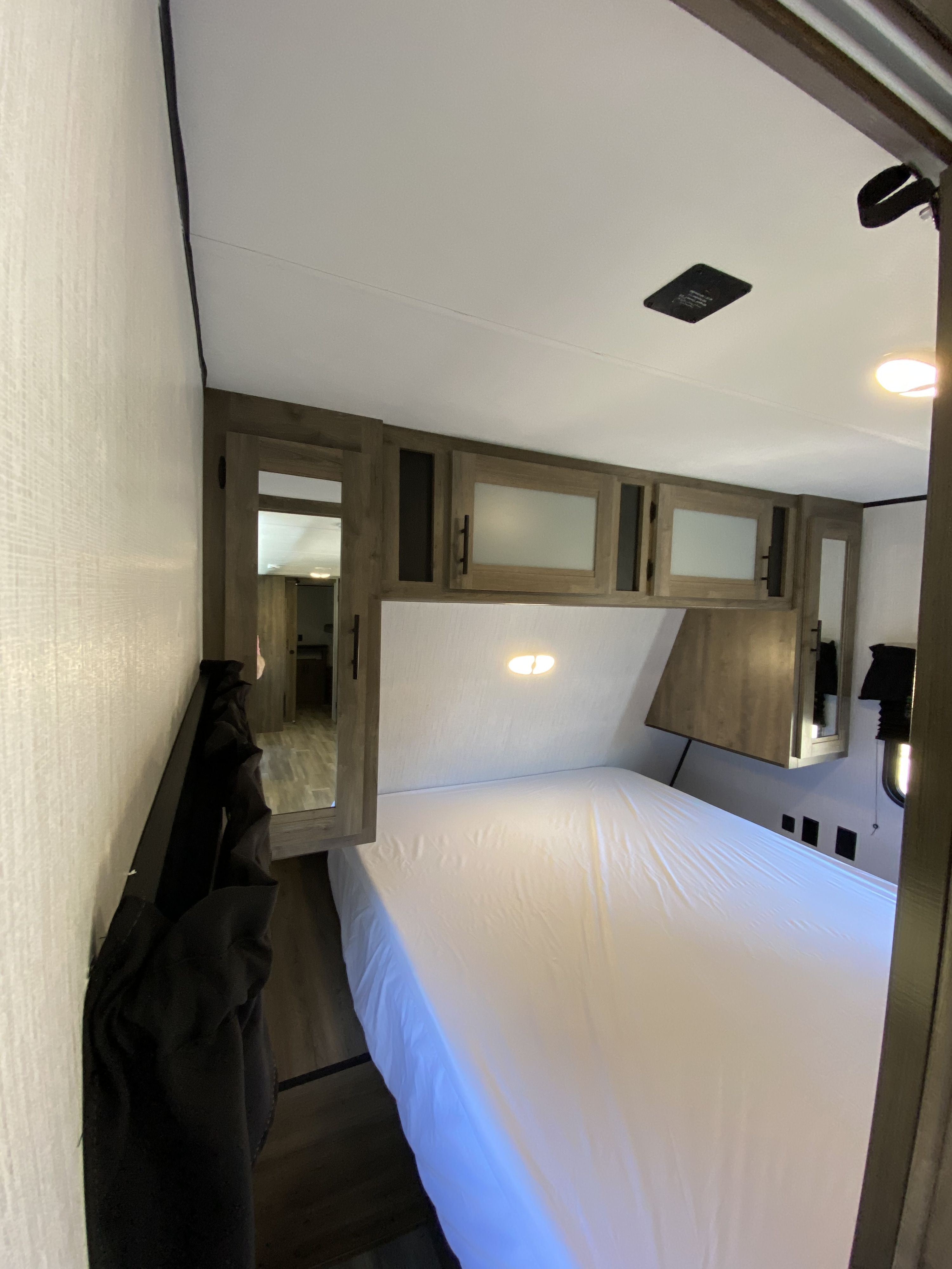 RV rental bedroom with a large white-sheeted bed, overhead cabinets, wall-mounted light, and wooden accents.. Heartland Pioneer 2021