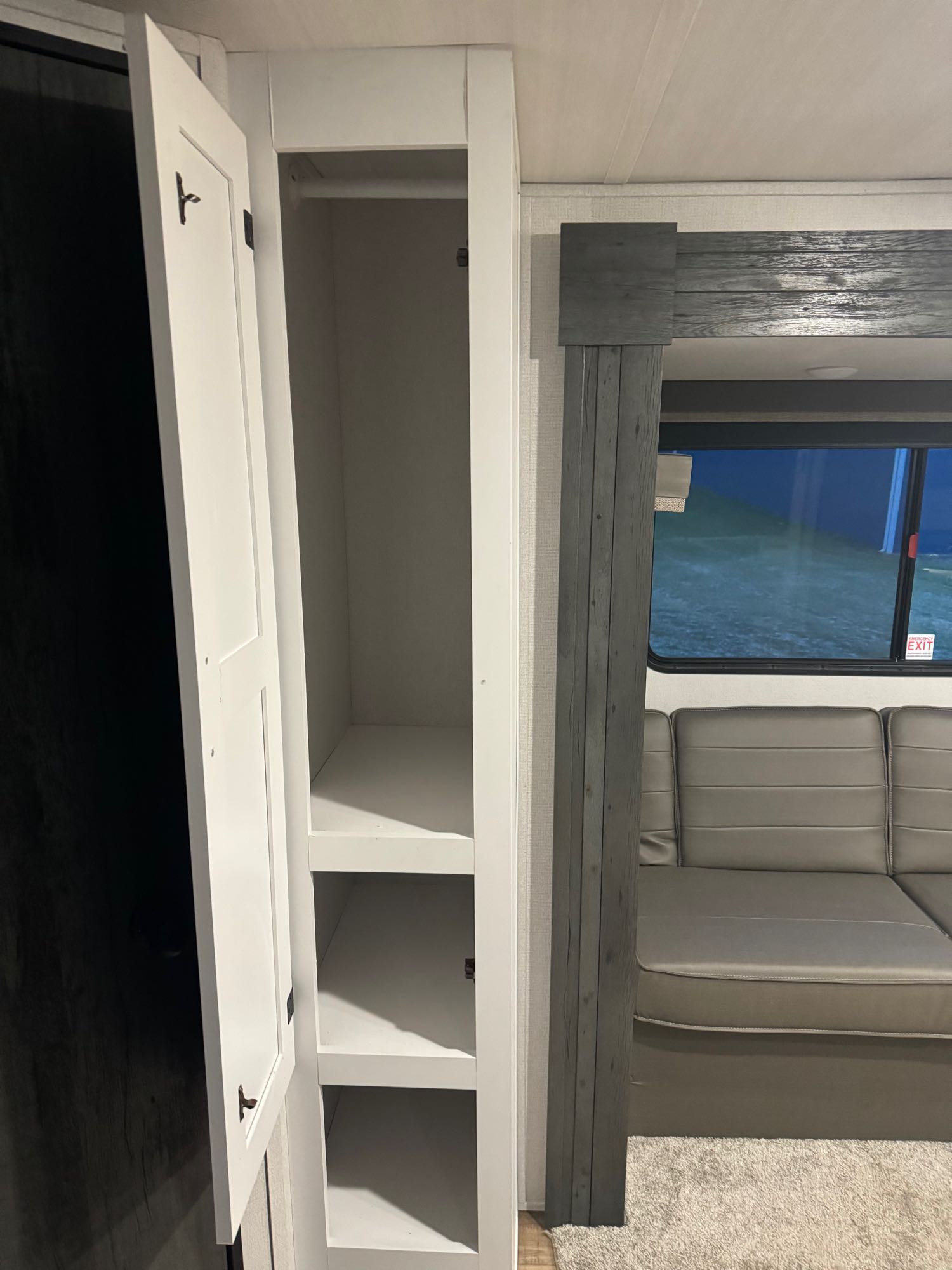 RV rental interior: open white cabinet with storage shelves & hanging rod, plus sofa and window.. keystone hideout 2022