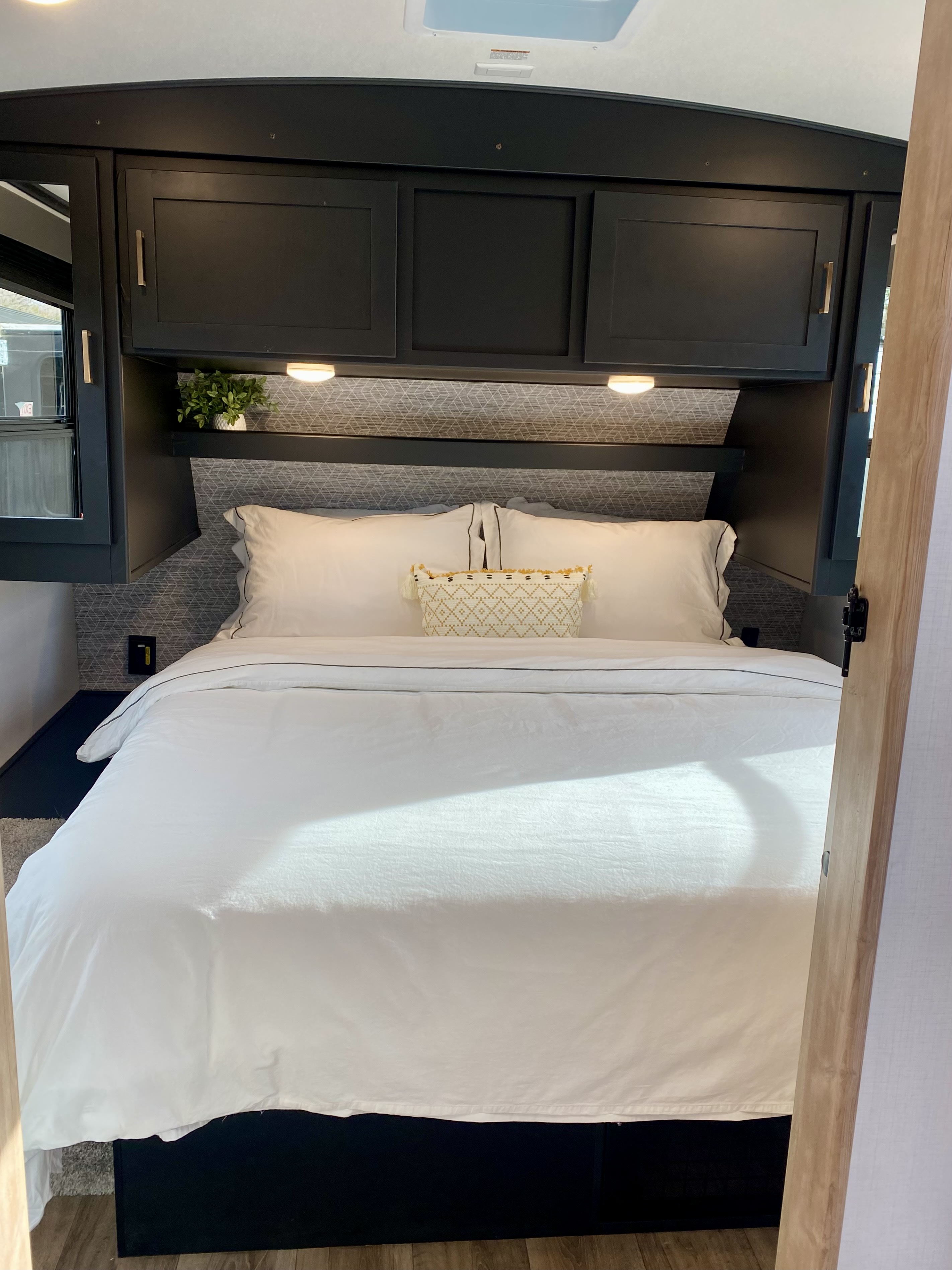 Modern RV rental bedroom featuring a pristine white bed, dark overhead cabinets, and stylish patterned headboard.. Keystone RV Outback Ultra-Lite 2022