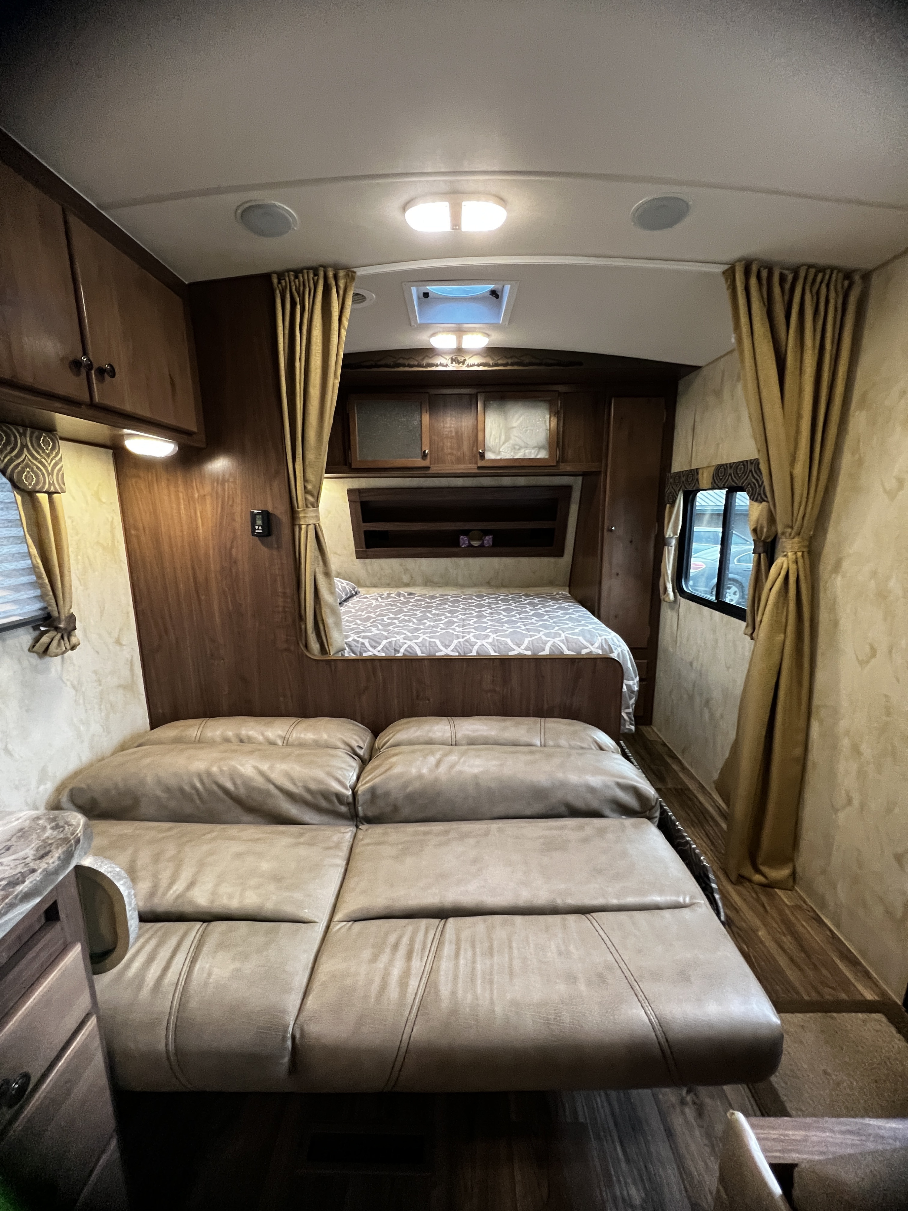 Cozy RV rental interior: rear bed with patterned comforter, leather-like sofa, wood trim & cabinets. Comfortable living space.. Nash 22H 2021