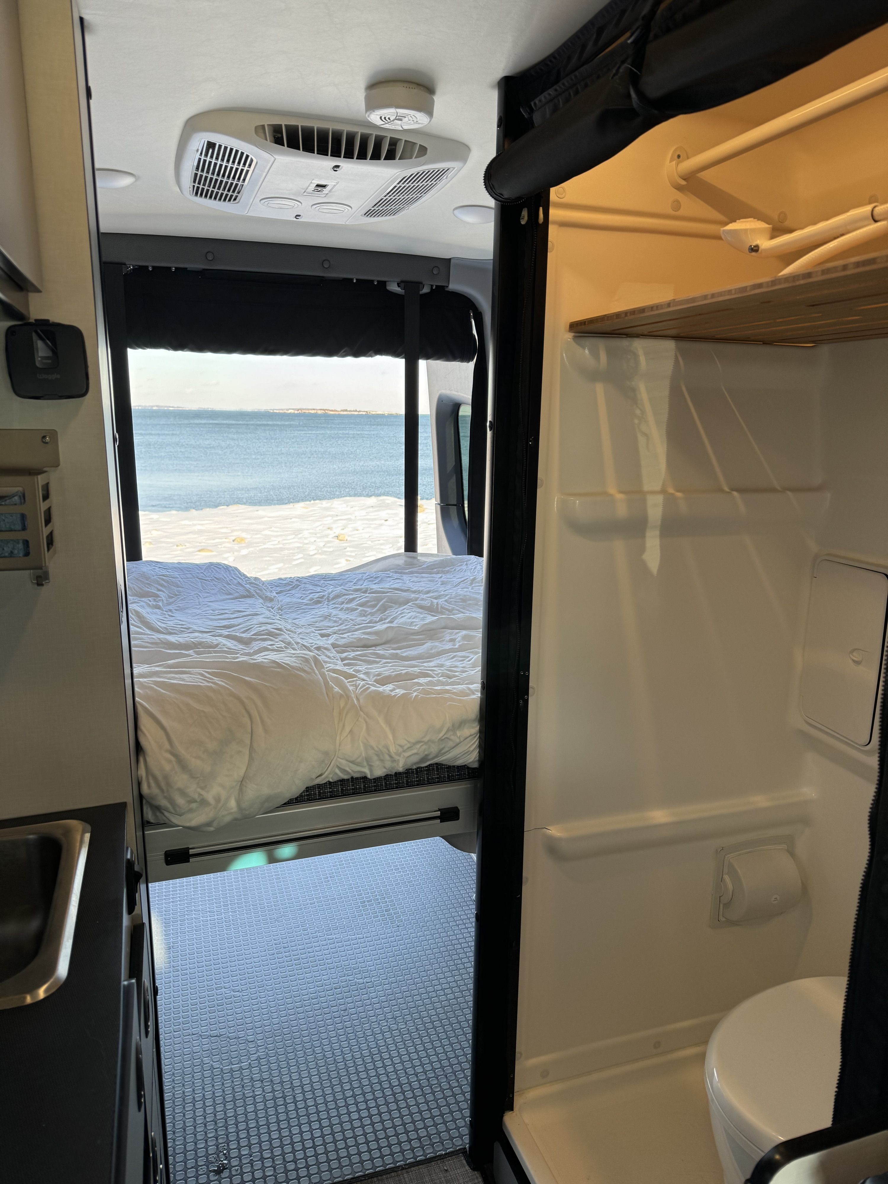 Cozy rv rental interior with a bed overlooking a snowy beach & ocean, featuring a sink area & compact bathroom.. Winnebago Revel 2022