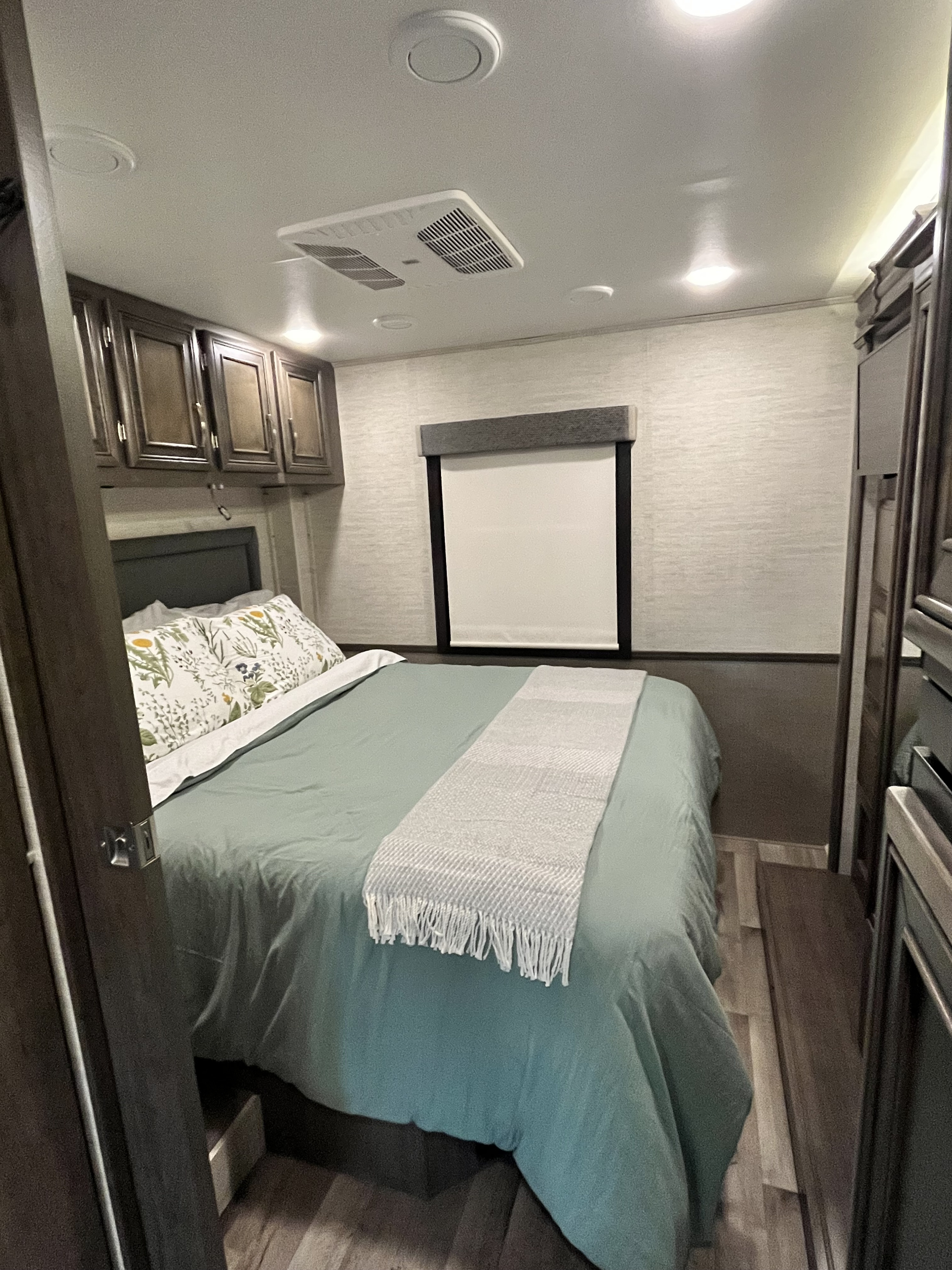 Experience comfort in this RV rental bedroom with a plush bed, green bedding, cabinets, and a window shade.. Jayco Alante 2023
