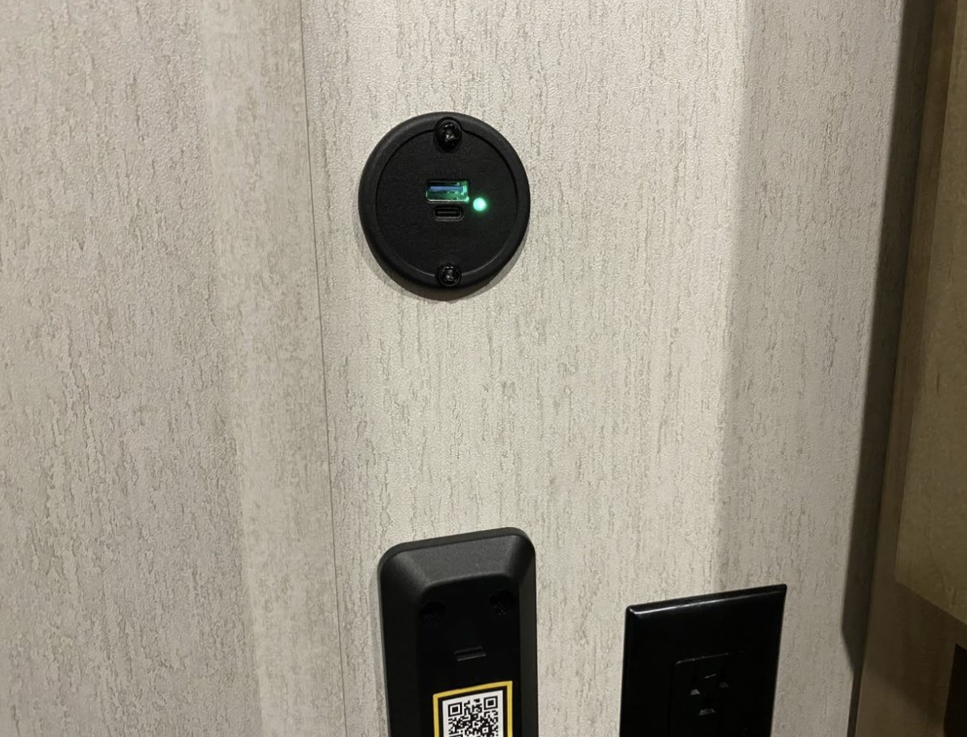 RV rental amenities: USB-A/C charging port with green light, control panel with QR code, and power outlet on a textured wall.. Forest River Cherokee Grey Wolf 2024