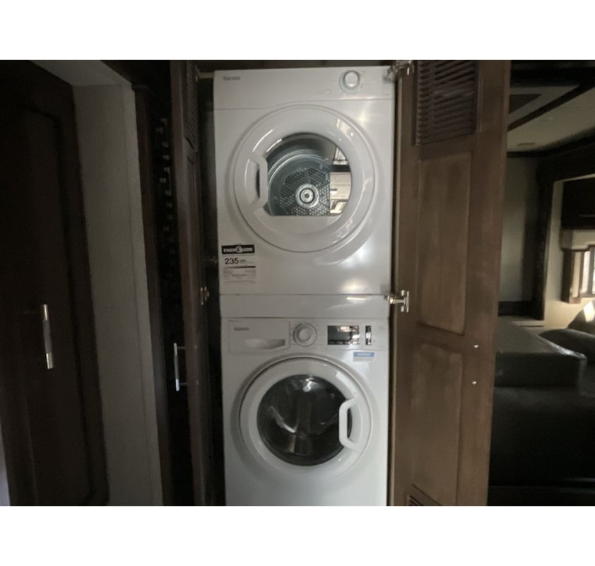 White stacked washer/dryer unit inside a compact space, a feature often found in an RV rental for easy laundry.. Newmar Ventana 2023