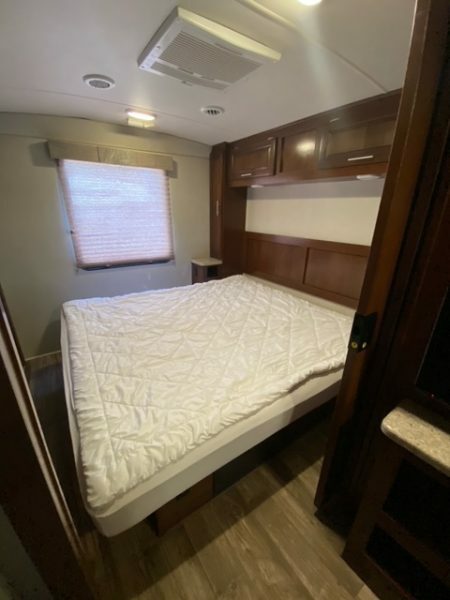 Comfortable rv rental bedroom featuring a bed, dark wood cabinetry, a window with blinds, and an AC unit.. FR3 FR3 Motorhome 2018