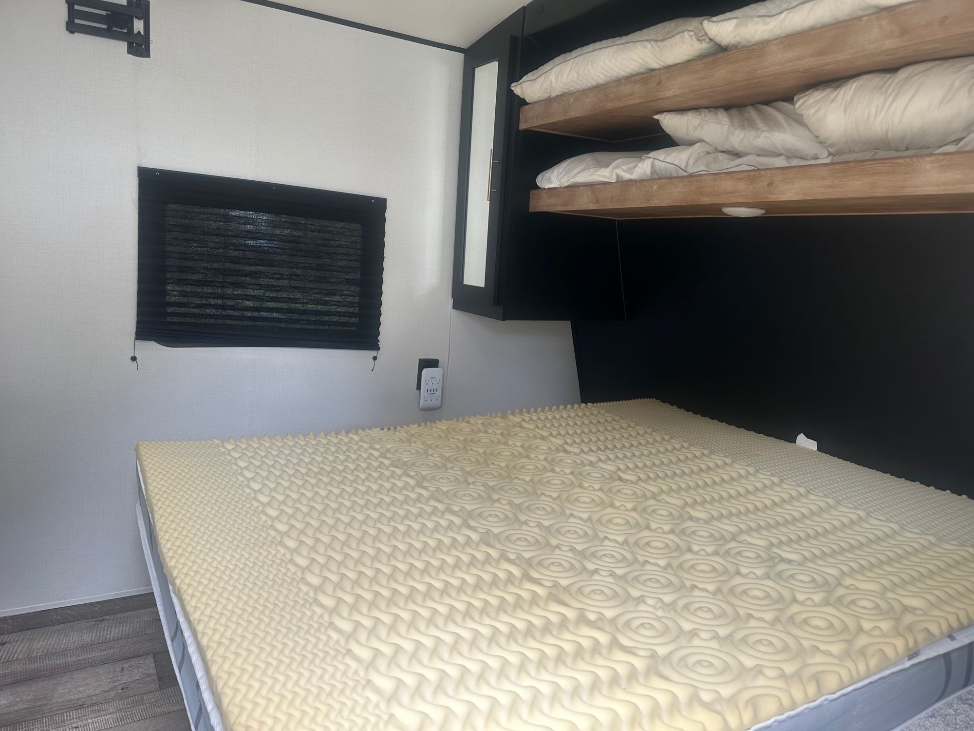 Compact RV rental bedroom featuring main bed with foam topper, two wooden bunk beds, and wall-mounted TV bracket.. Keystone RV Springdale 2022