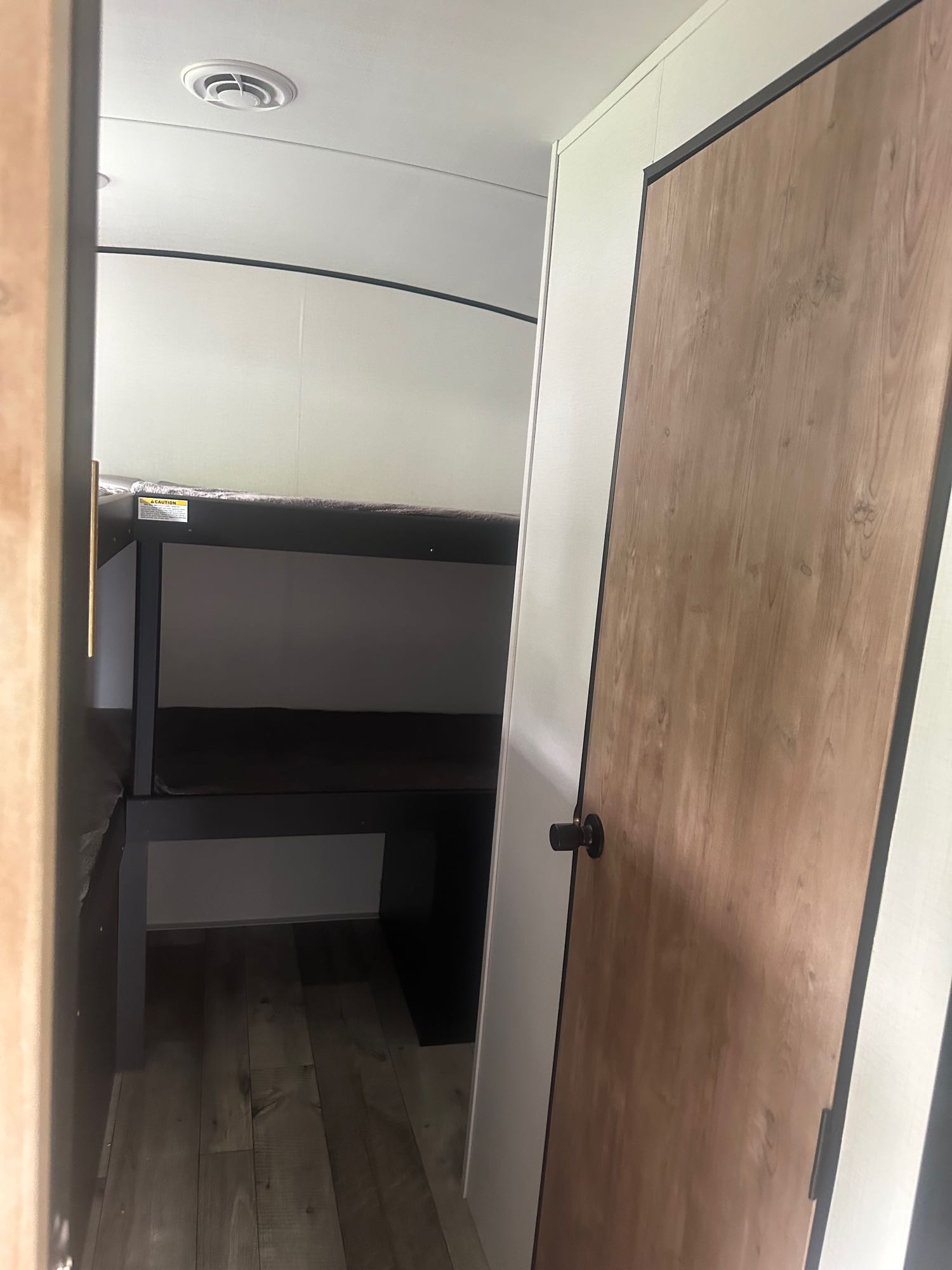 RV rental interior: Compact space with dark-framed bunk beds, a safety sticker, and a light wood-grain door on the right.. Keystone RV Springdale 2022