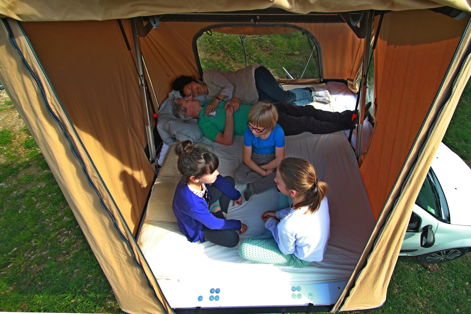 A family relaxes inside a rooftop tent, part of an RV rental, offering comfort during their outdoor adventure.. NaïtUp Hussarde Family 5 personnes 2024