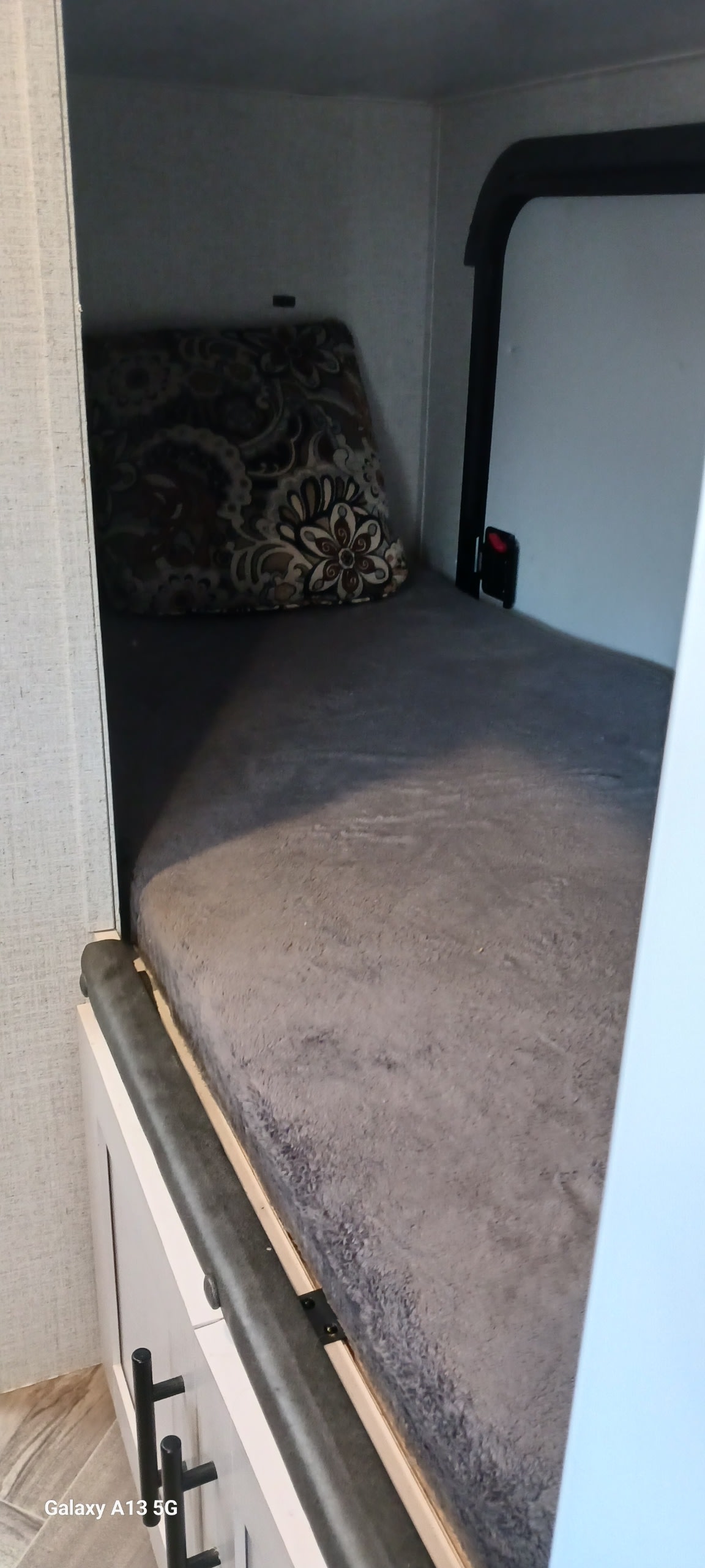 Compact RV rental bunk bed with grey mattress and patterned pillow, ready for a cozy sleep.. Dutchmen Coleman Rubicon 2021