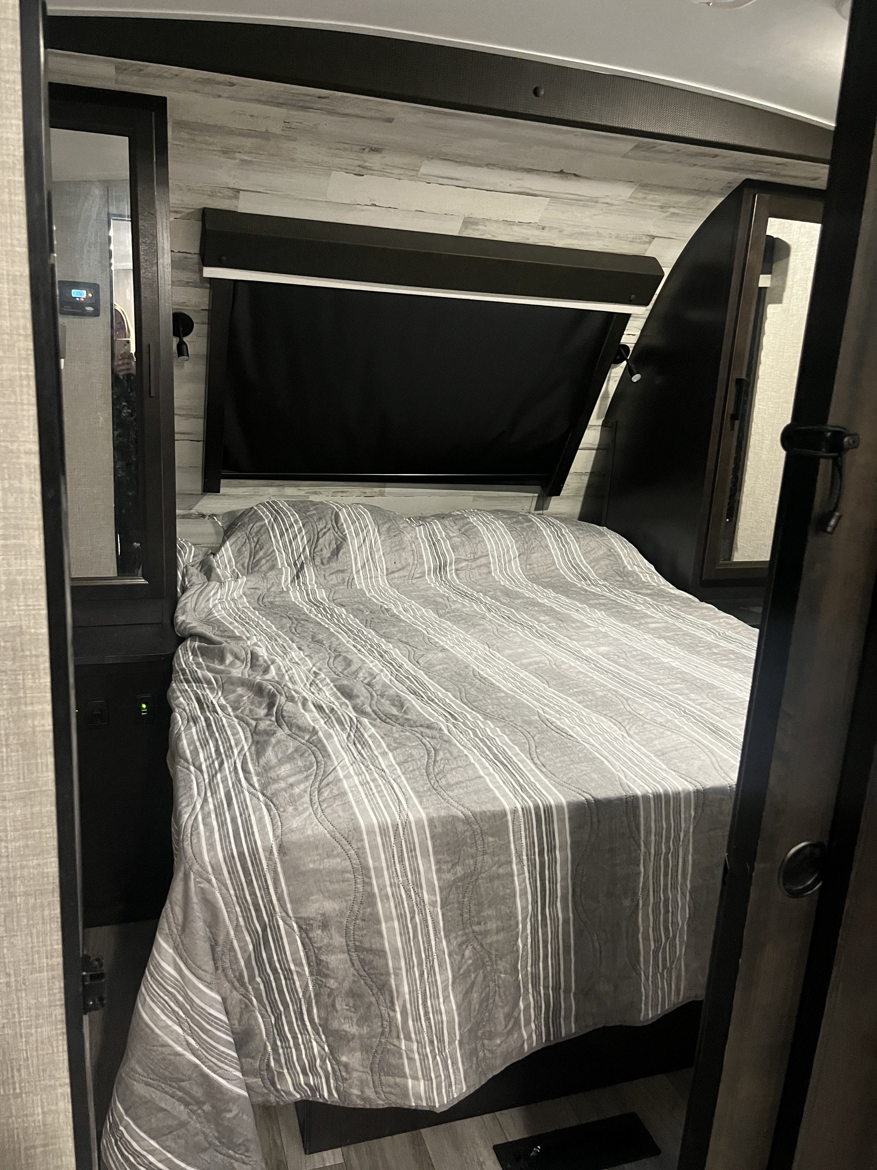 View of a well-appointed RV rental bedroom, featuring a comfortable striped bed, compact built-ins, and dark window blinds.. Jayco White Hawk 2022