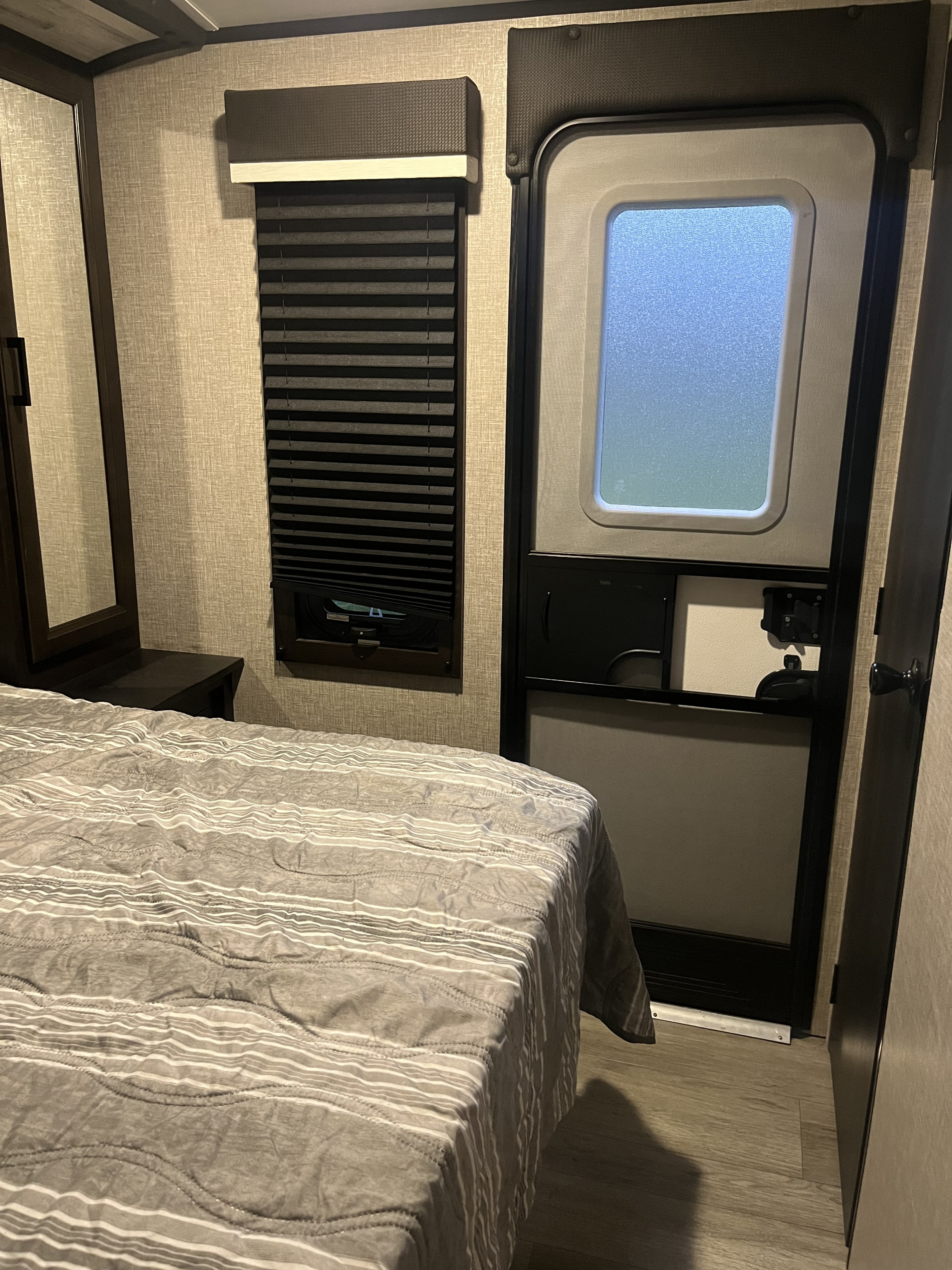 Cozy RV rental bedroom with striped comforter, window blinds, and an RV door, offering comfort.. Jayco White Hawk 2022