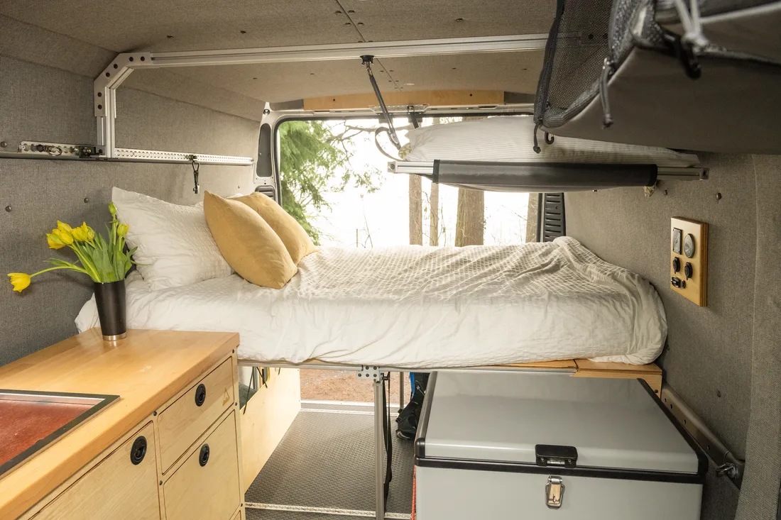 Explore this comfy RV rental camper van interior. Elevated bed, sink, fridge, and handy overhead storage for travel.. Ram Promaster 2500 2019