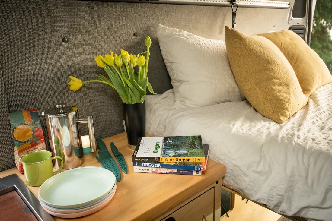 Experience comfort in this RV rental. Bed, French press, tulips, & Oregon travel guides inside a camper van.. Ram Promaster 2500 2019