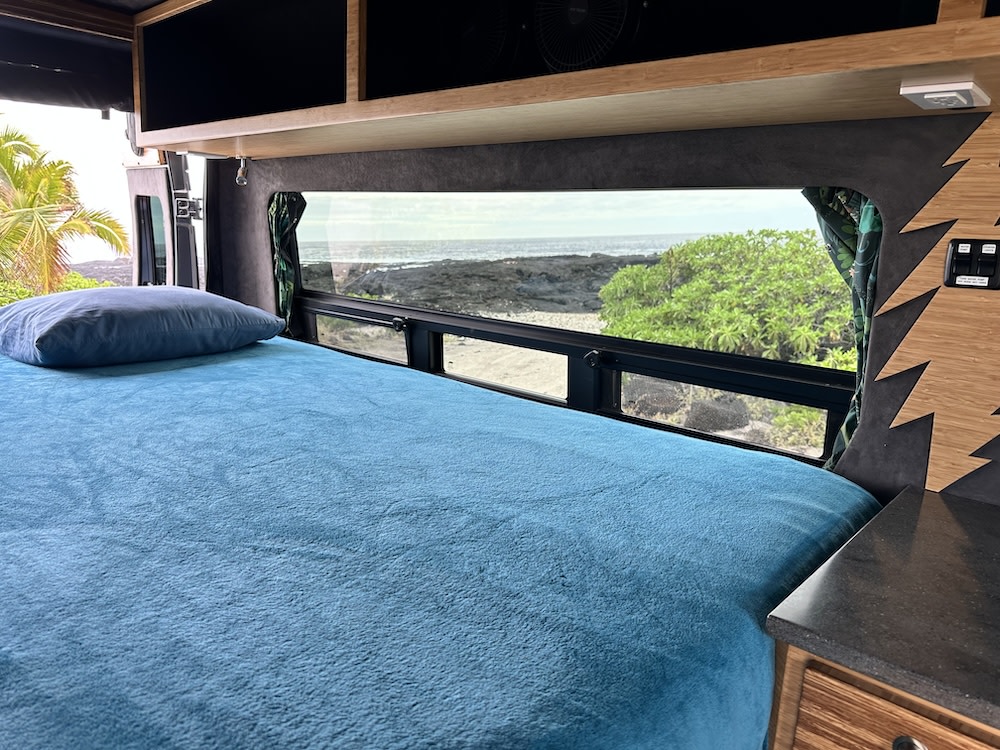 Experience comfort in this RV rental! Inside, a bed offers a clear ocean view from the camper van's window.. Ram Promaster 2017