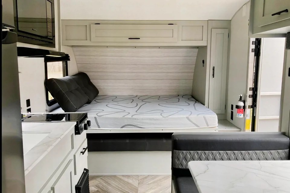 Bright RV rental interior showcasing a cozy bed with overhead storage, a compact kitchen, and a dinette.. Forest River Salem FSX 2021