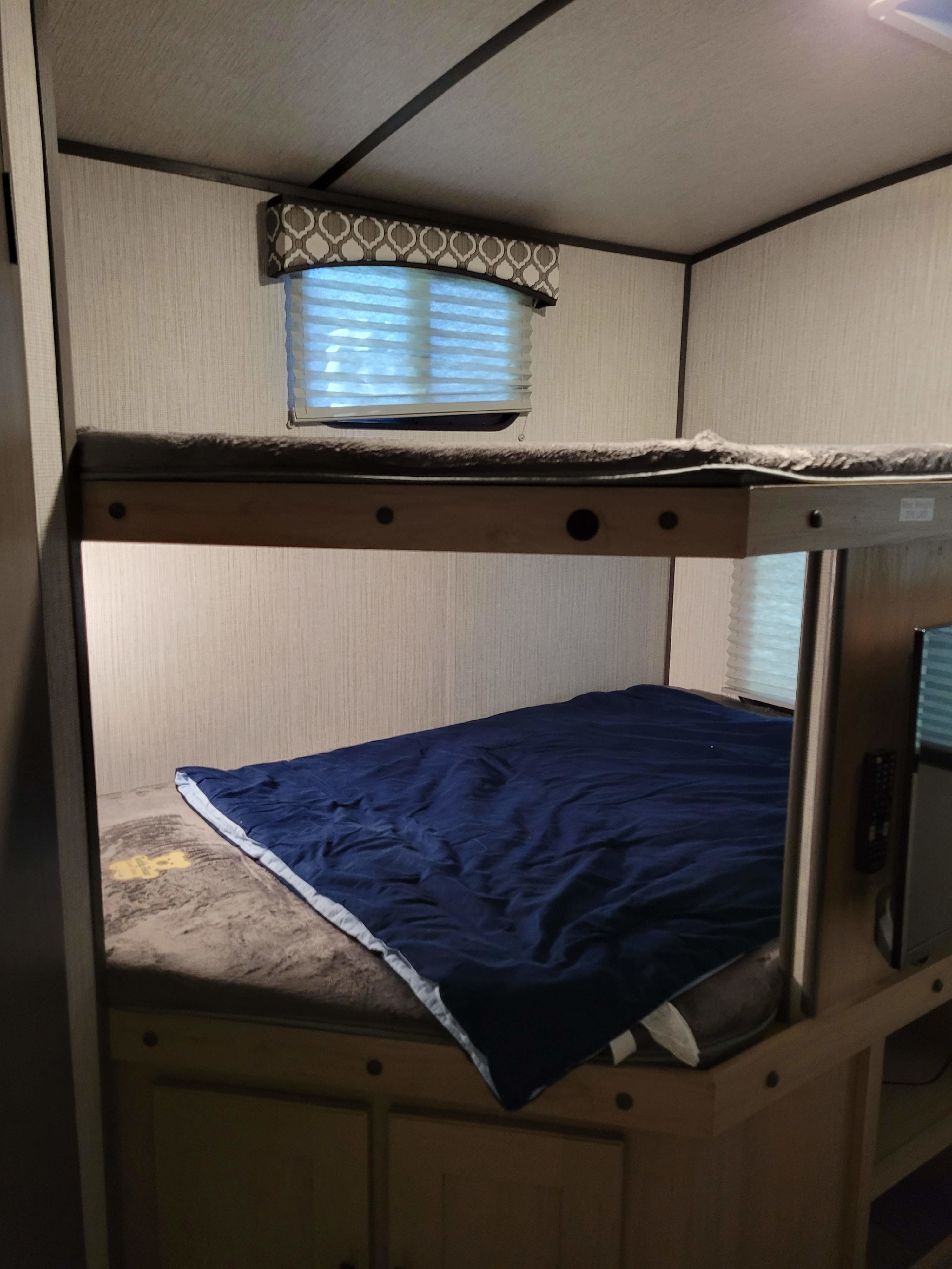 Cozy RV rental bedroom featuring comfortable bunk beds, with a lower bed dressed in a blue blanket and an upper bunk visible.. Cruiser RV Radiance 2021