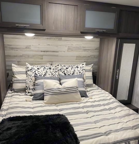 Cozy RV rental bedroom with striped bedding, light wood wall, and frosted glass overhead cabinets.. Dutchmen Kodiak Ultra Lite 2020