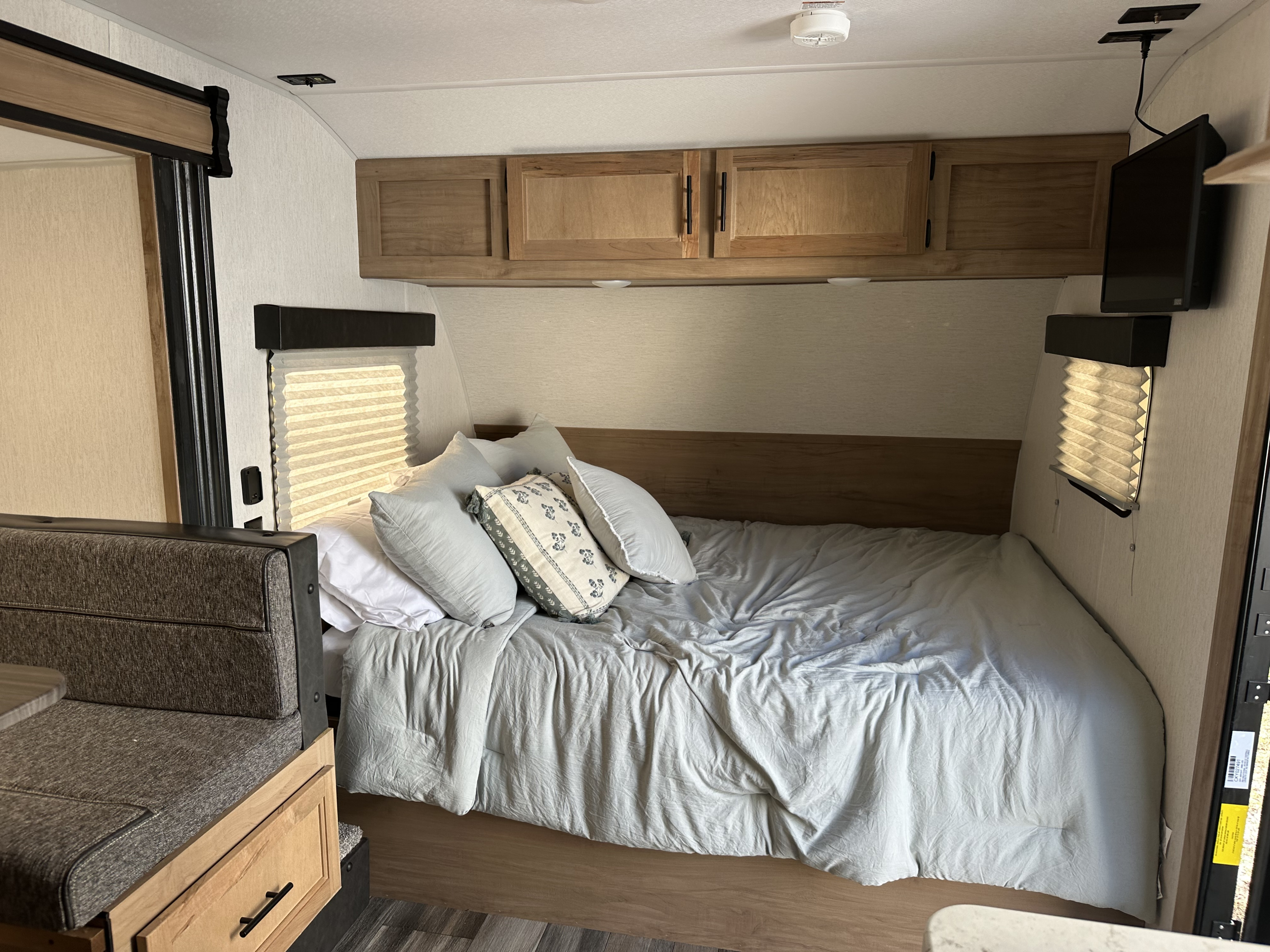 Inside an RV rental: a comfortable bedroom area with light grey bedding, overhead storage, and a dinette.. Forest River Cherokee Wolf Pup 2023