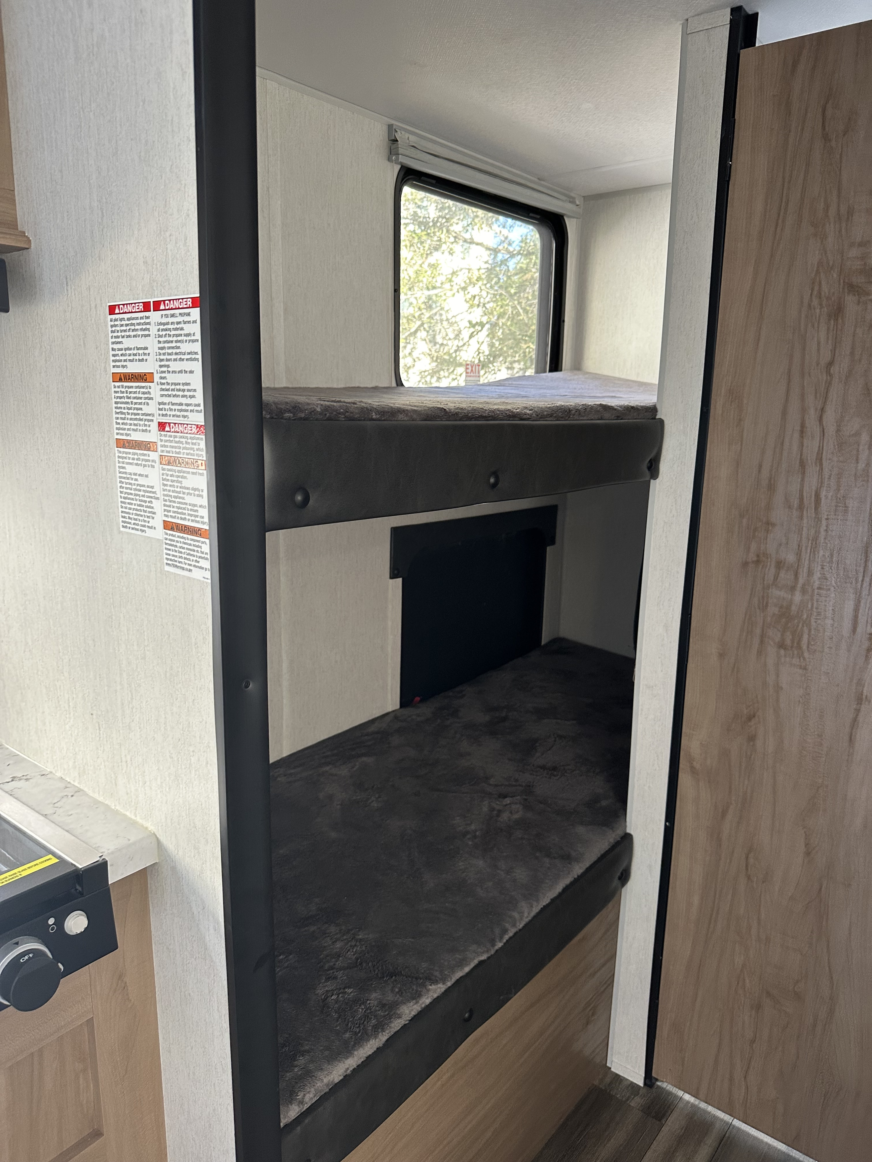 Inside RV rental: stacked bunk beds, a window, part of a kitchen counter with a stove, and safety warnings on the wall.. Forest River Cherokee Wolf Pup 2023